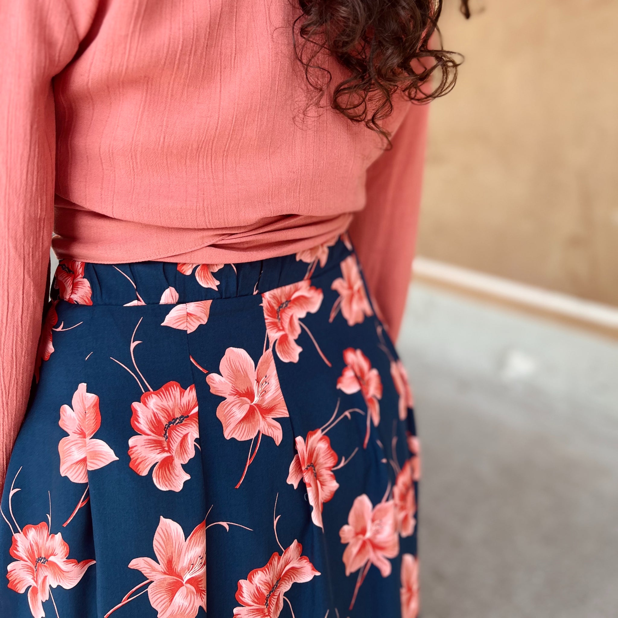 Person trägt ein rosa Oberteil und einen blauen Rock mit rosa Blumenmuster, im Innenraum aufgenommen.