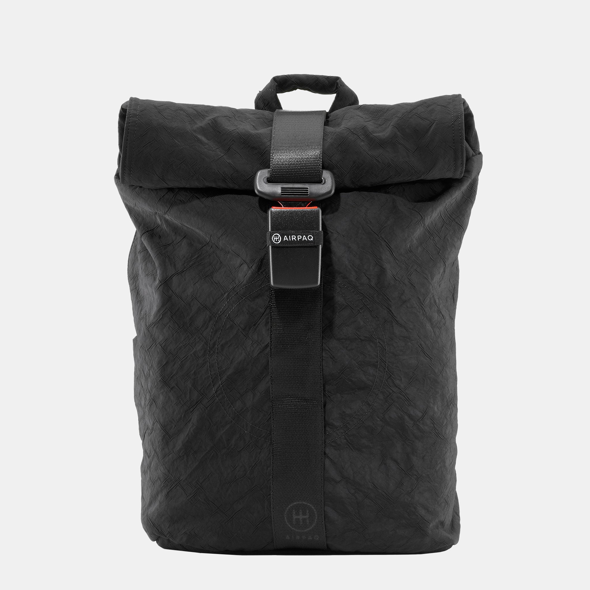 Ein schwarzer Rolltop-Rucksack mit Schnallenverschluss auf der Vorderseite und einem kleinen Airpaq-Logo auf dem Gurt, der auf einem schlichten weißen Hintergrund abgebildet ist.