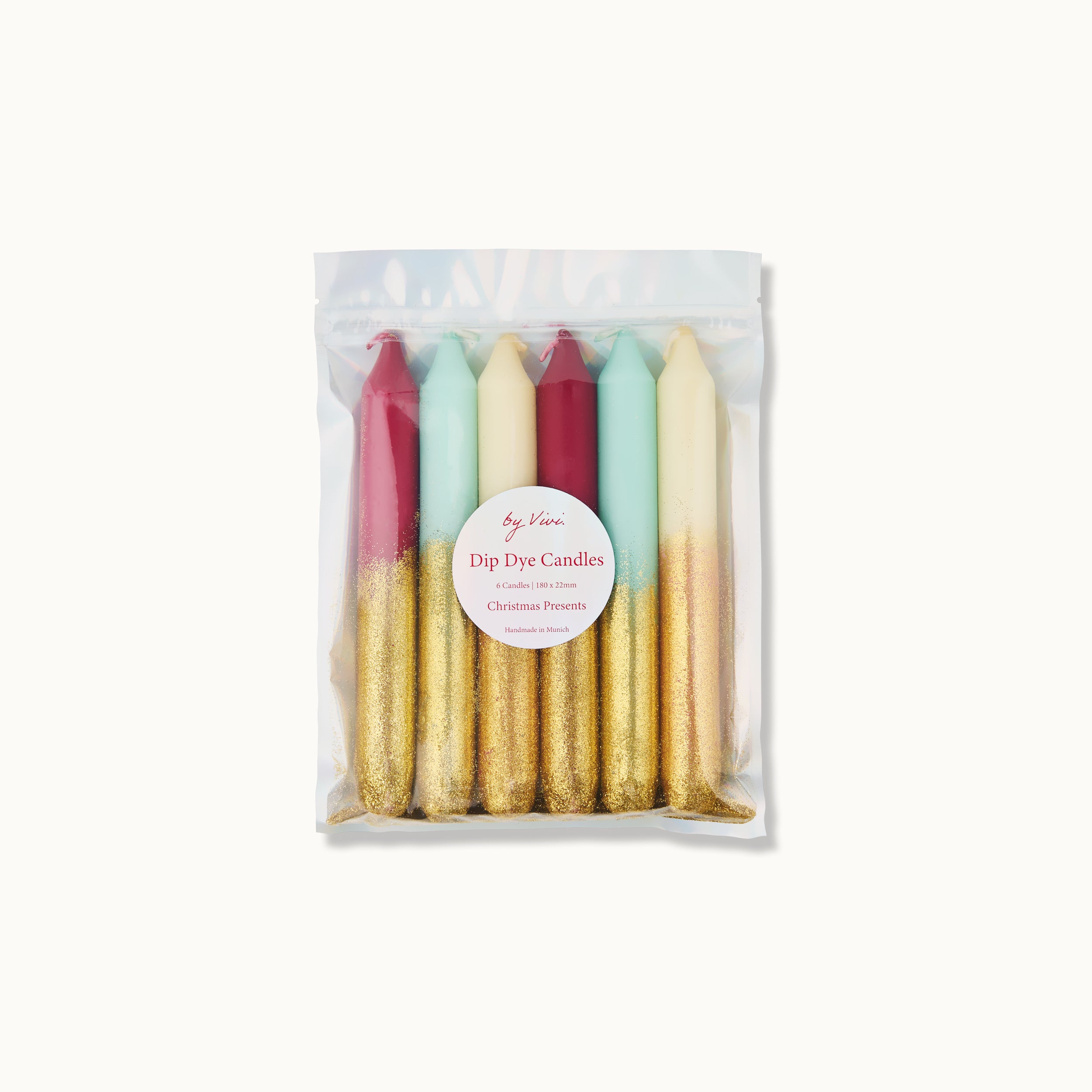 Eine durchsichtige Plastiktüte mit sechs Kerzen in den Farben Rot, Mintgrün und Weiß, jeweils mit goldfarbenen Böden. Auf einem runden Etikett auf der Tüte steht "Dip Dye Candles - Christmas Presents".