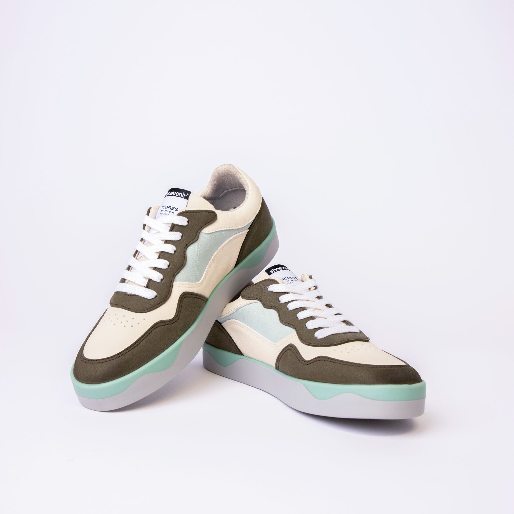 Ein Paar modische Turnschuhe mit weißen, hellgrauen und olivgrünen Einsätzen, weißen Schnürsenkeln und hellblau-grünen Sohlen, die vor einem schlichten weißen Hintergrund stehen.