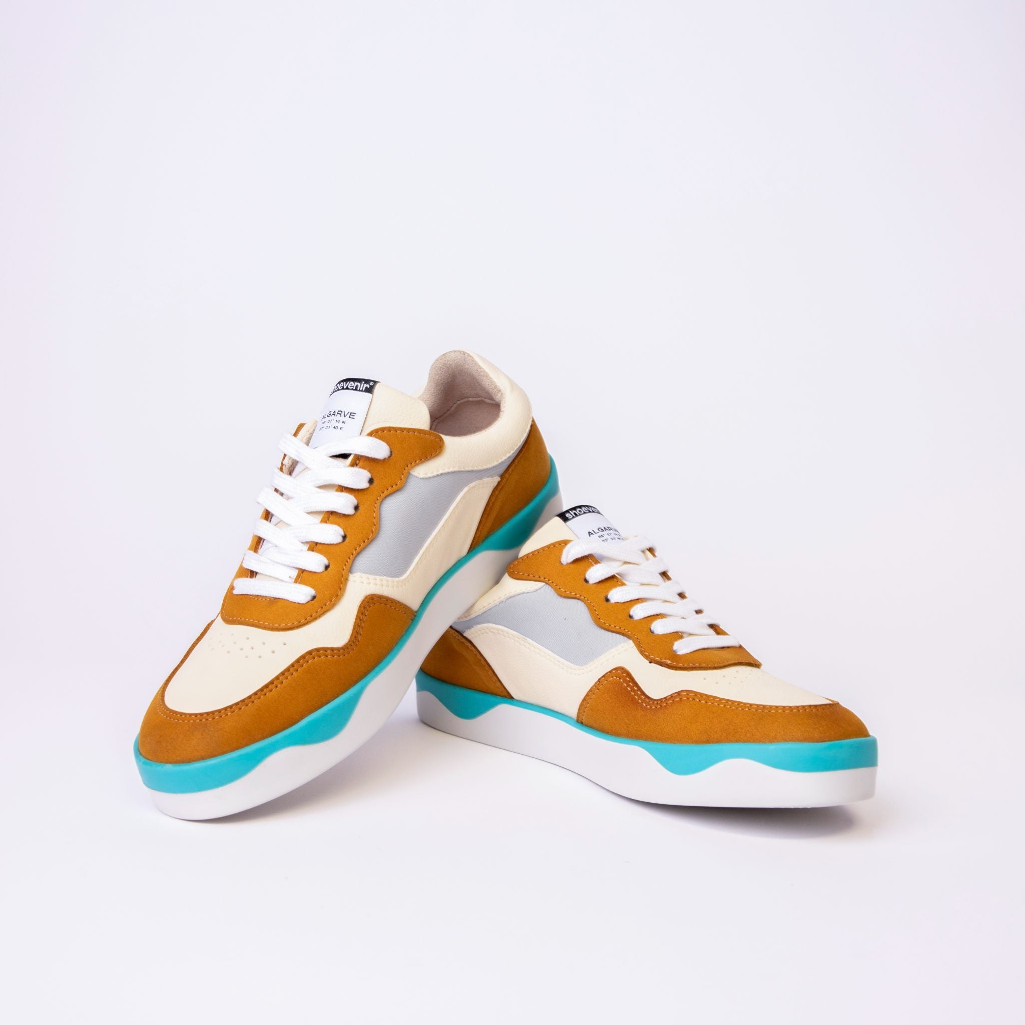 Ein Paar modische Turnschuhe mit senfgelben, weißen und hellgrauen Einsätzen, einer blaugrünen Zierleiste an der Sohle und weißen Schnürsenkeln, die vor einem schlichten weißen Hintergrund stehen.