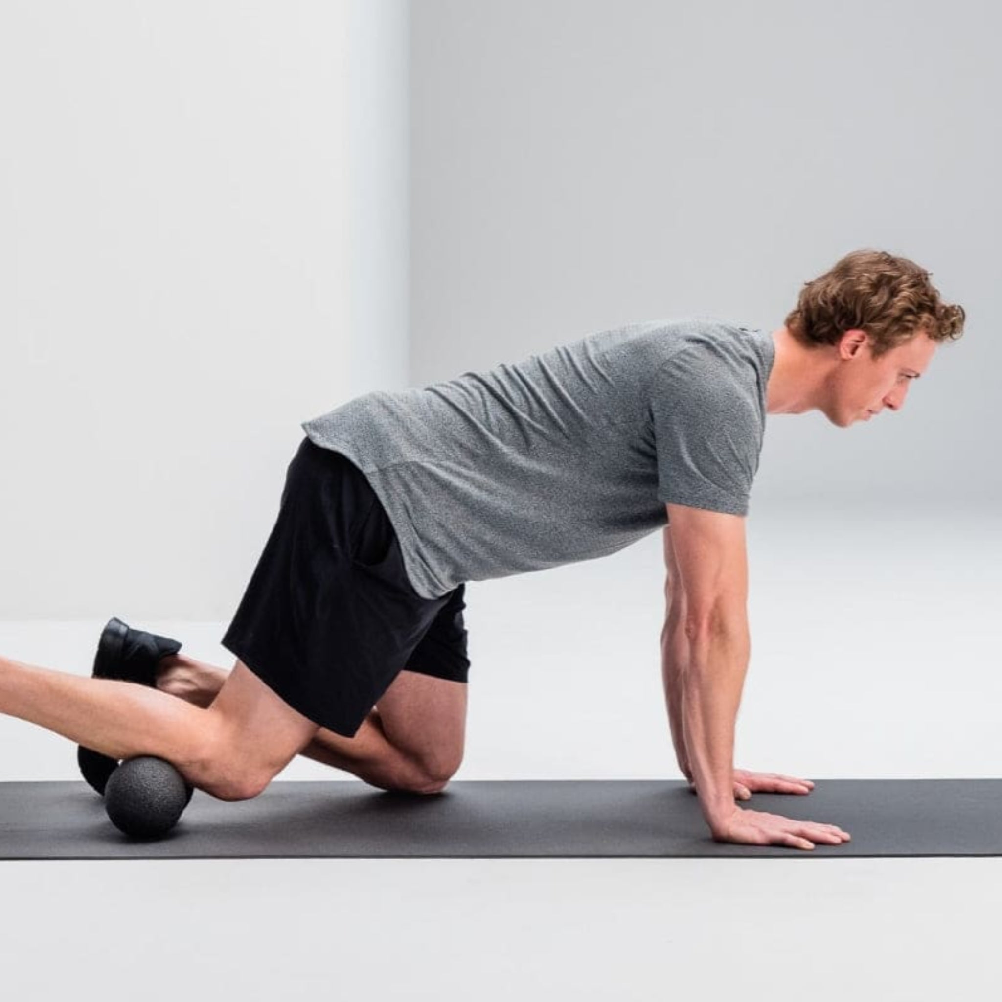 Ein Mann macht eine Fitnessübung auf einer Matte, kniend mit einem Schaumstoffball unter den Knien.