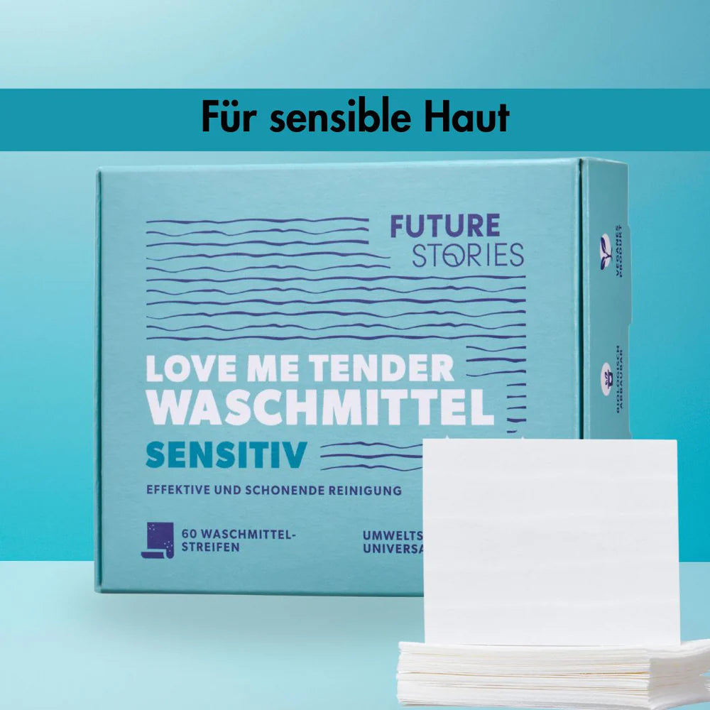 Eine Schachtel Future Stories Love Me Tender sensitive Waschmittel mit 60 Waschmittelstreifen ist auf blauem Hintergrund abgebildet. Ein Stapel weißer Waschmittelstreifen ist vor der Schachtel platziert. Der Text lautet Für sensible Haut.