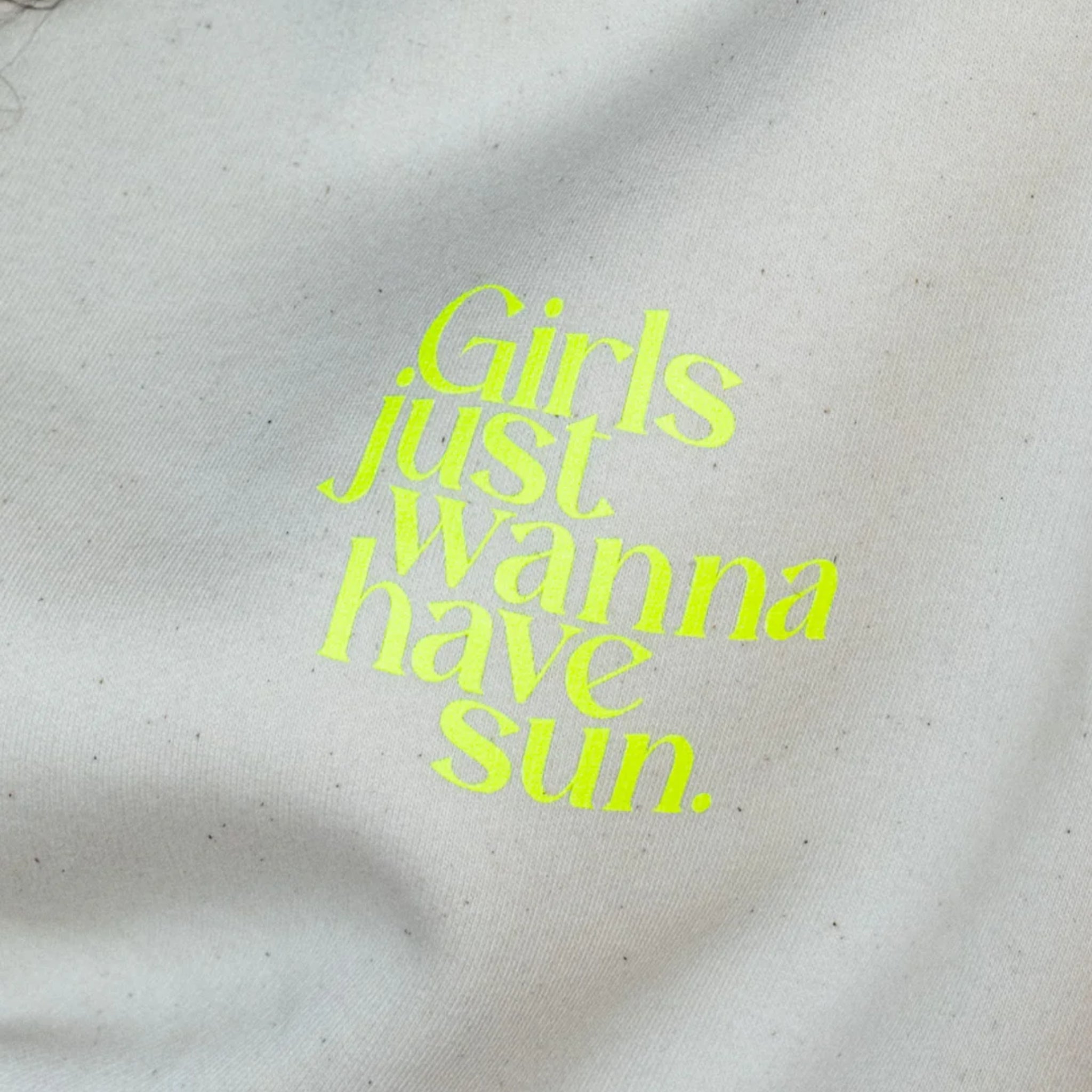 Nahaufnahme eines hellen Stoffes mit leuchtend gelber Schrift, die lautet: Girls just wanna have sun.