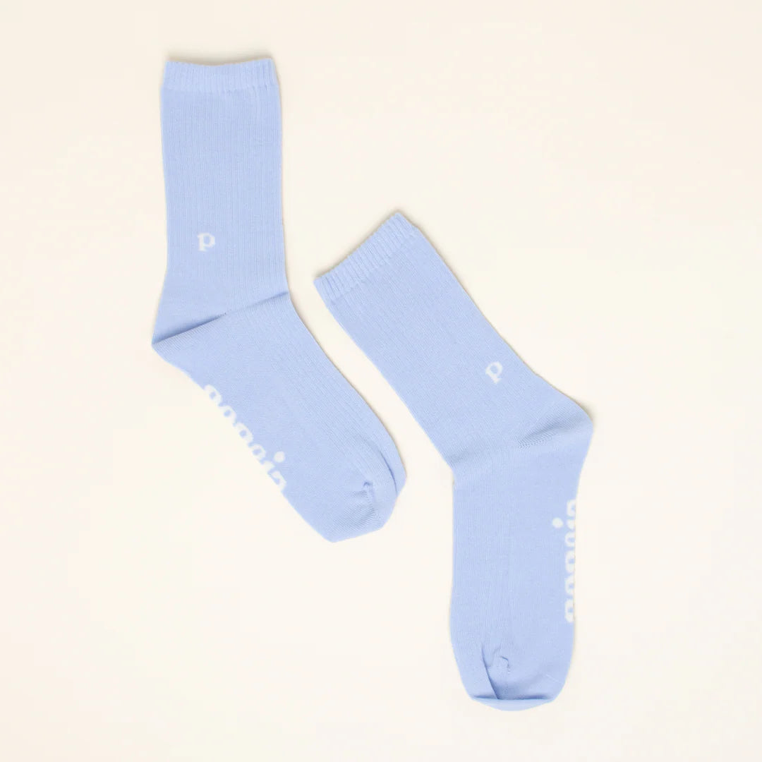 Ein Paar hellblaue Socken mit einem kleinen weißen "p" am Knöchel und weißem Text entlang der Sohle auf einem einfarbig beigen Hintergrund.