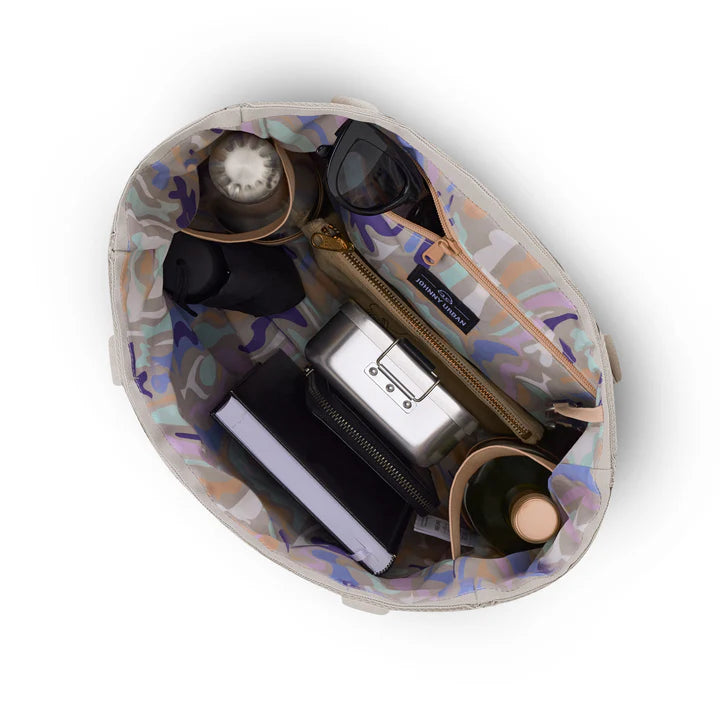 Draufsicht auf eine offene Tragetasche mit farbenfrohem Innenraum, in dem sich ein Notizbuch, eine Wasserflasche, eine Sonnenbrille, eine Lunchbox aus Metall, eine Brieftasche, ein Kaffeebecher und eine weitere Flasche befinden.