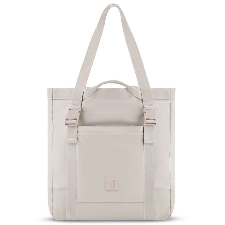 Eine hellbeige Tragetasche mit langen Schulterriemen, einem kurzen Tragegriff, einer Vordertasche mit zwei vertikalen Schnallen und einem kleinen quadratischen Logoaufnäher im unteren Bereich.