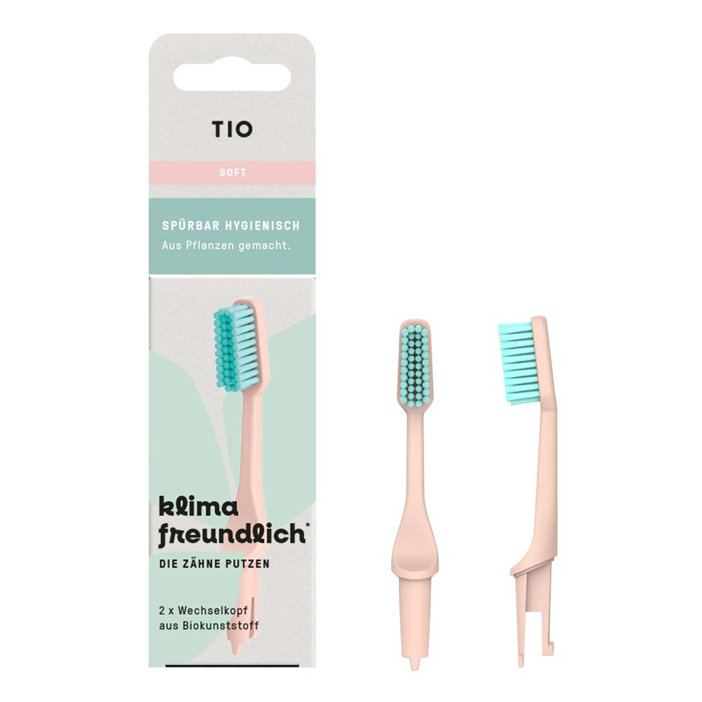 Eine Packung TIO-Zahnbürstenköpfe aus pflanzlichen Materialien mit zwei pastellrosa Ersatzköpfen mit grünen Borsten, abgebildet neben der Produktverpackung mit deutschem Text.