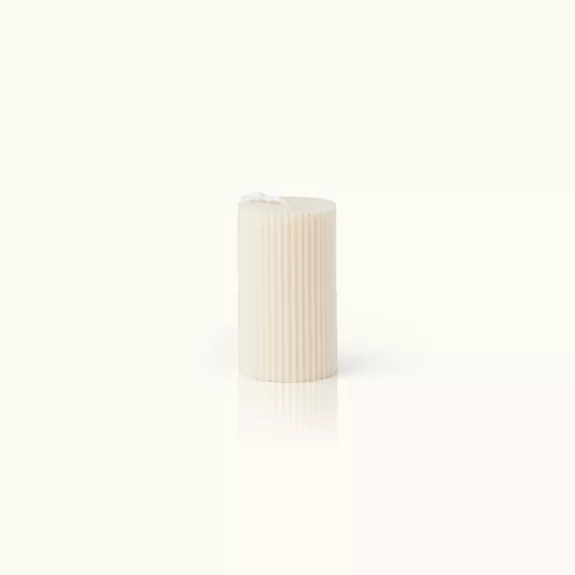 Beige geriffelte Stumpenkerze vor weißem Hintergrund.
