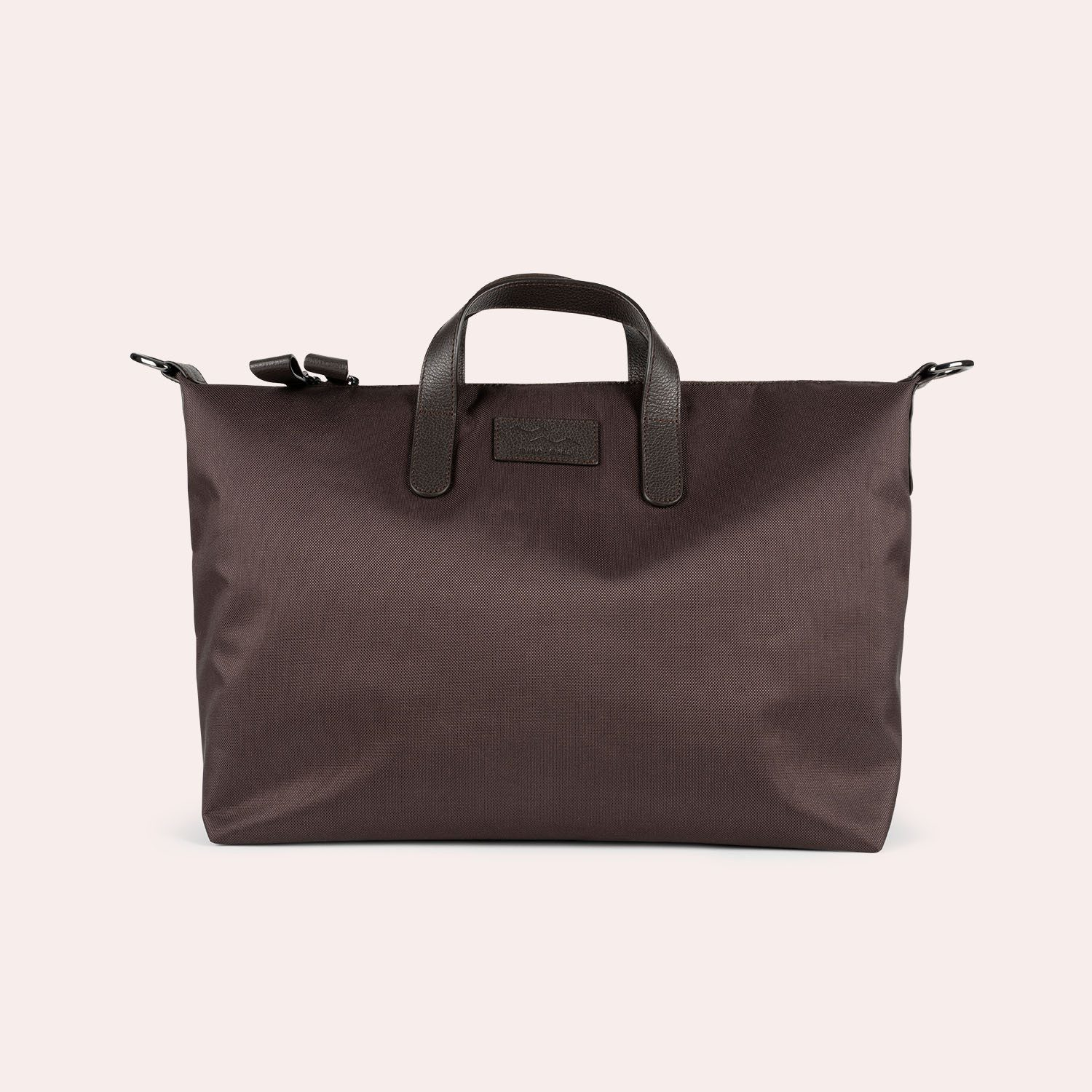 Eine große, dunkelbraune Tragetasche mit kurzen schwarzen Ledergriffen und einem abnehmbaren Schulterriemen vor einem schlichten hellen Hintergrund.