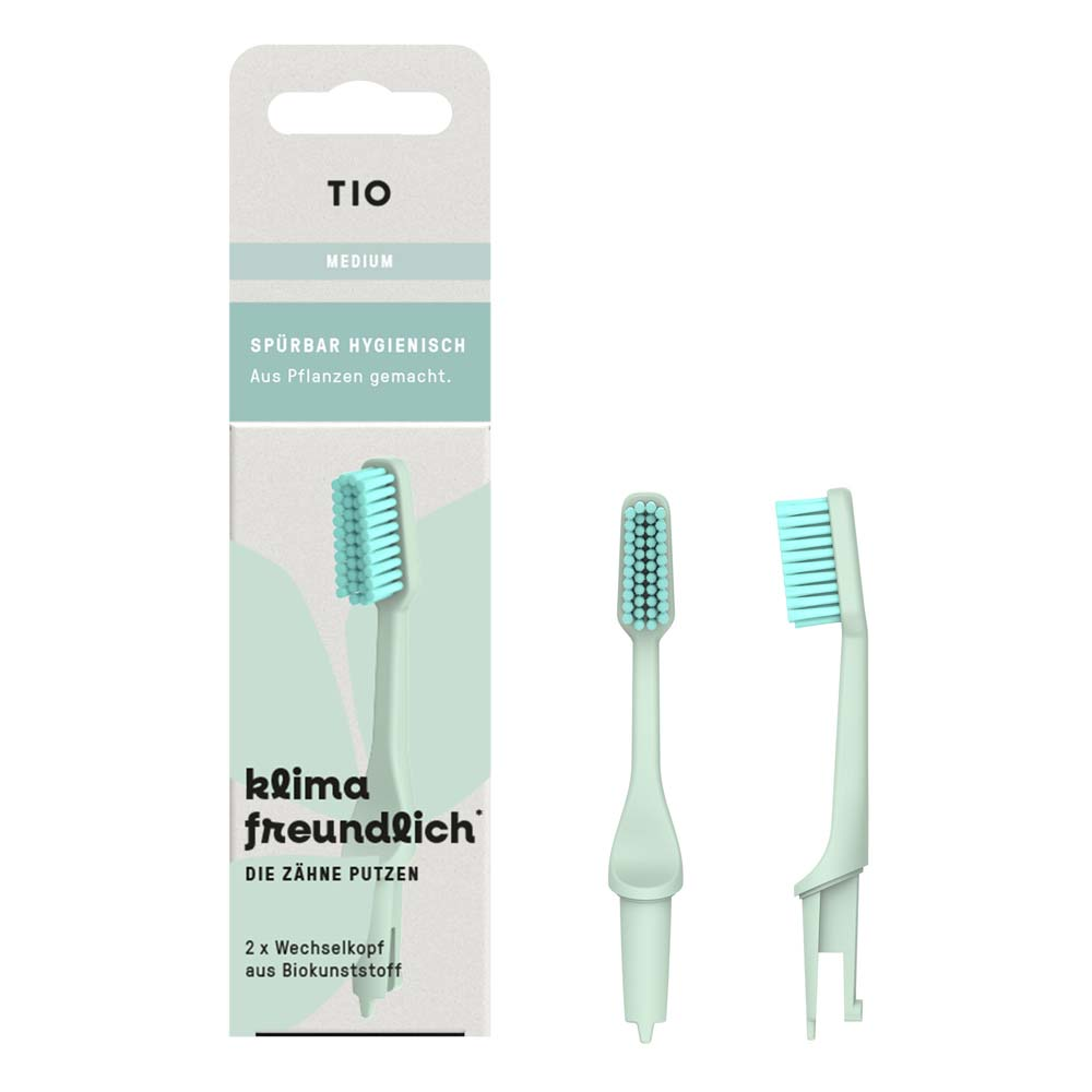 Eine hellgrüne Zahnbürste und zwei Ersatzbürstenköpfe werden neben einer umweltfreundlichen Verpackung mit der Aufschrift TIO und klimafreundlich gezeigt. Die Verpackung hebt pflanzliche Materialien und mittlere Borsten hervor.