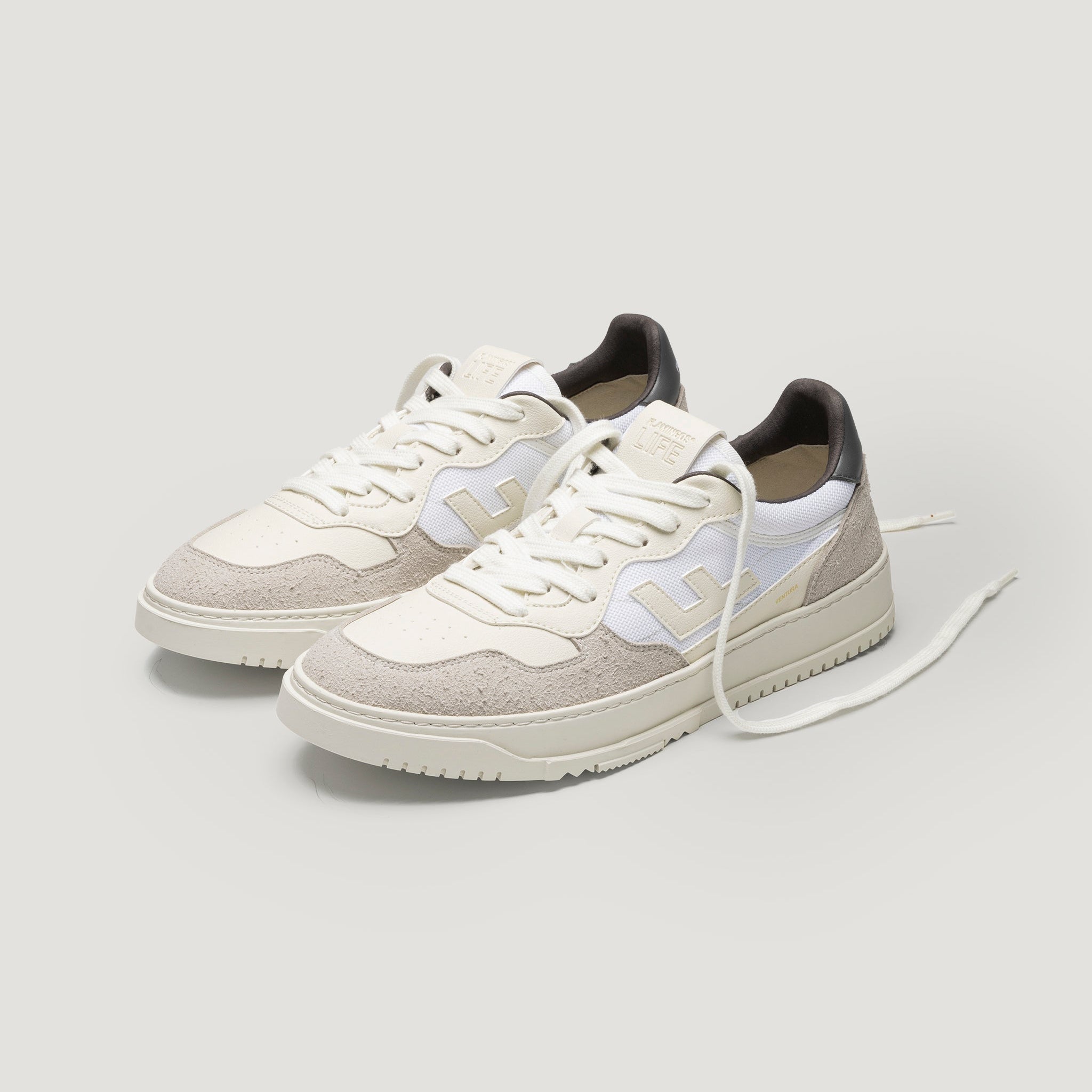 Ein Paar stilvolle weiße und beigefarbene Turnschuhe mit weißen Schnürsenkeln, Wildleder- und Mesh-Texturen und hellgrauen Akzenten, dargestellt auf einem sauberen weißen Hintergrund.