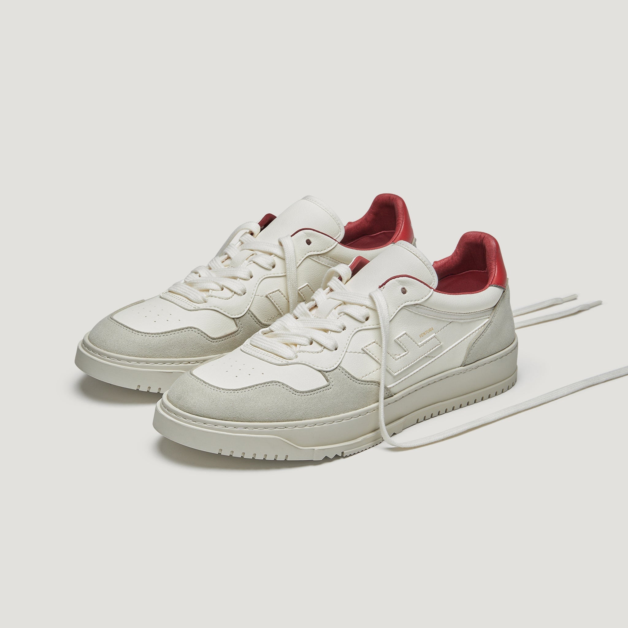 Ein Paar weiße und cremefarbene Turnschuhe mit rotem Innenfutter, weißen Sohlen und passenden weißen Schnürsenkeln vor einem schlichten weißen Hintergrund.