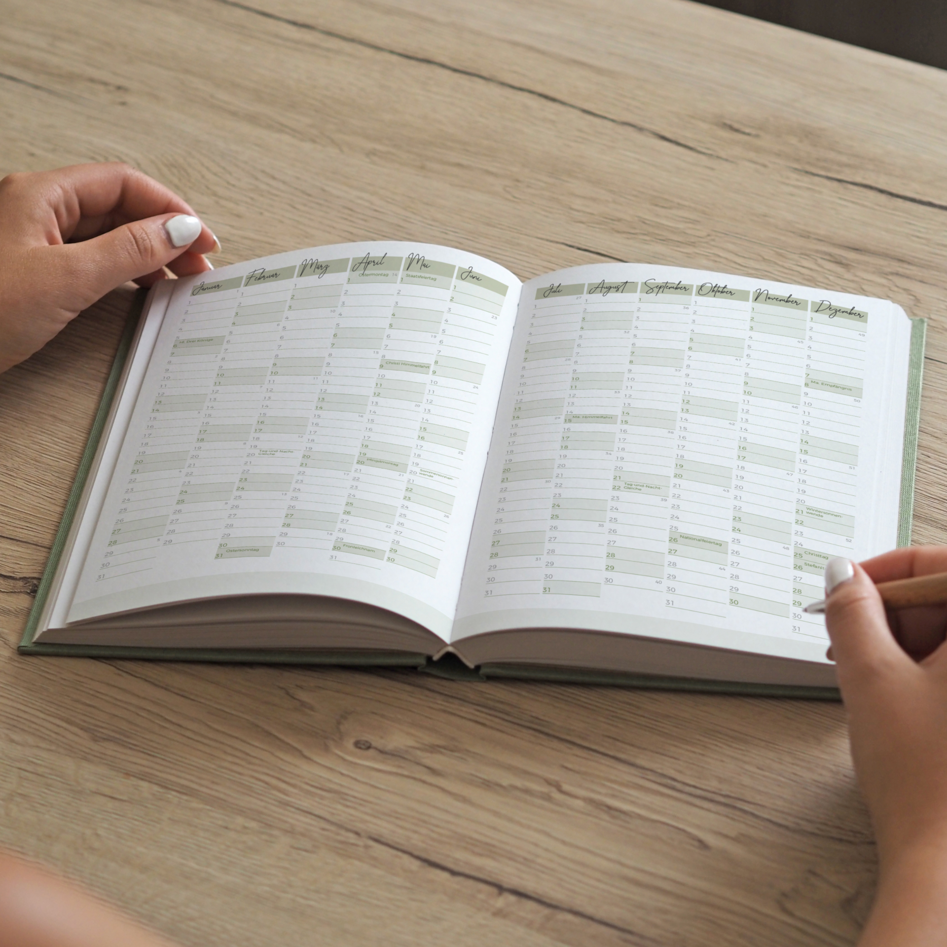 Person blättert in einem aufgeschlagenen Jahreskalender auf einem Holztisch.