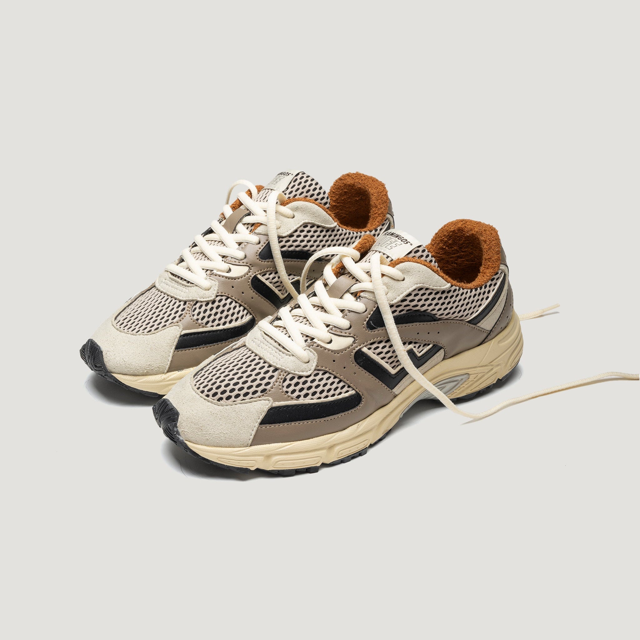 Ein Paar beigefarbene und braune Sportschuhe mit weißen Schnürsenkeln, Mesh-Obermaterial und hellbrauner Innenausstattung, die nebeneinander auf einem schlichten hellgrauen Hintergrund stehen.