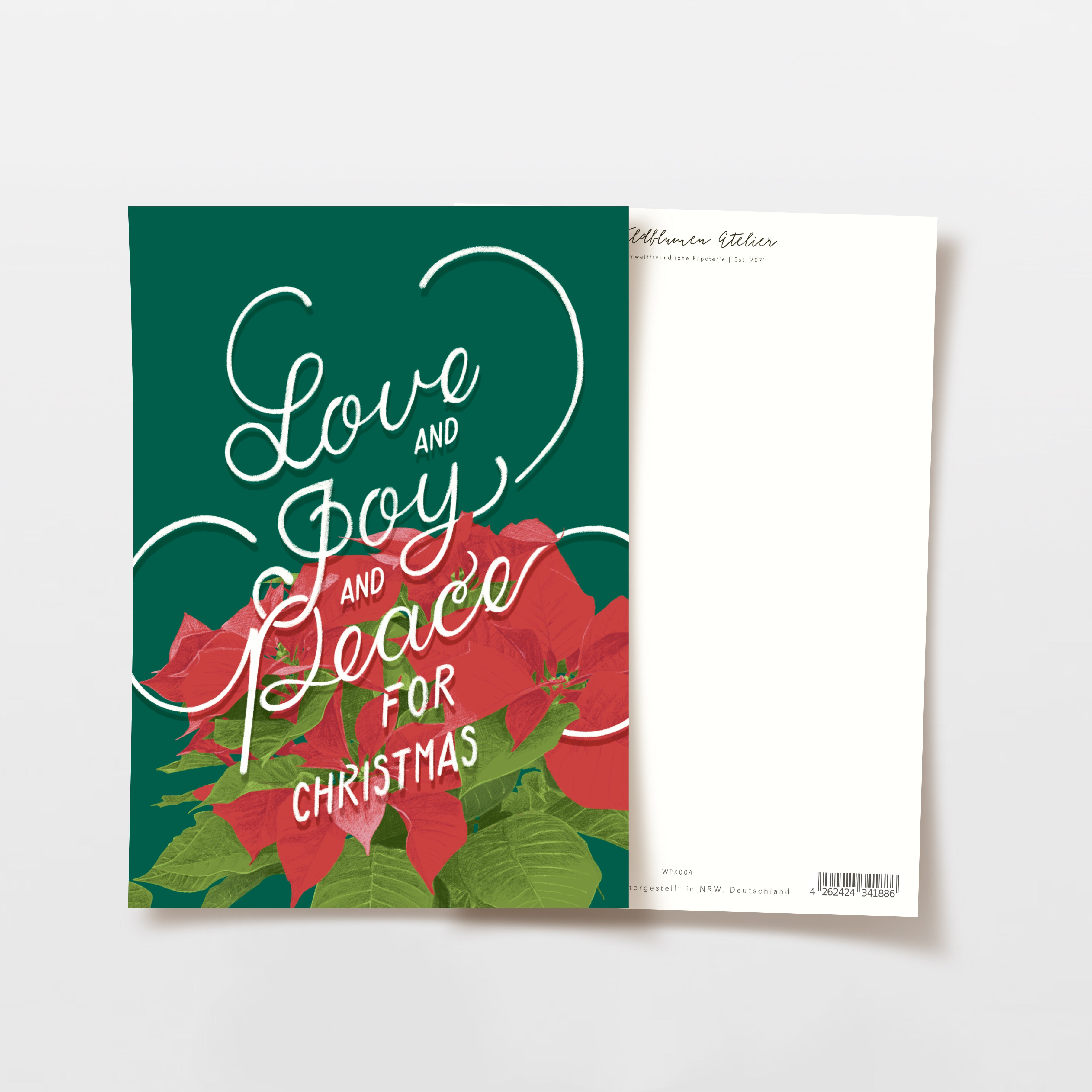 Eine Weihnachtskarte mit roten Weihnachtssternblüten und den Worten Love and Joy and Peace for Christmas in weißer Schrift auf grünem Hintergrund. Die Rückseite der Karte ist einfarbig weiß mit einem kleinen schwarzen Text am oberen Rand.