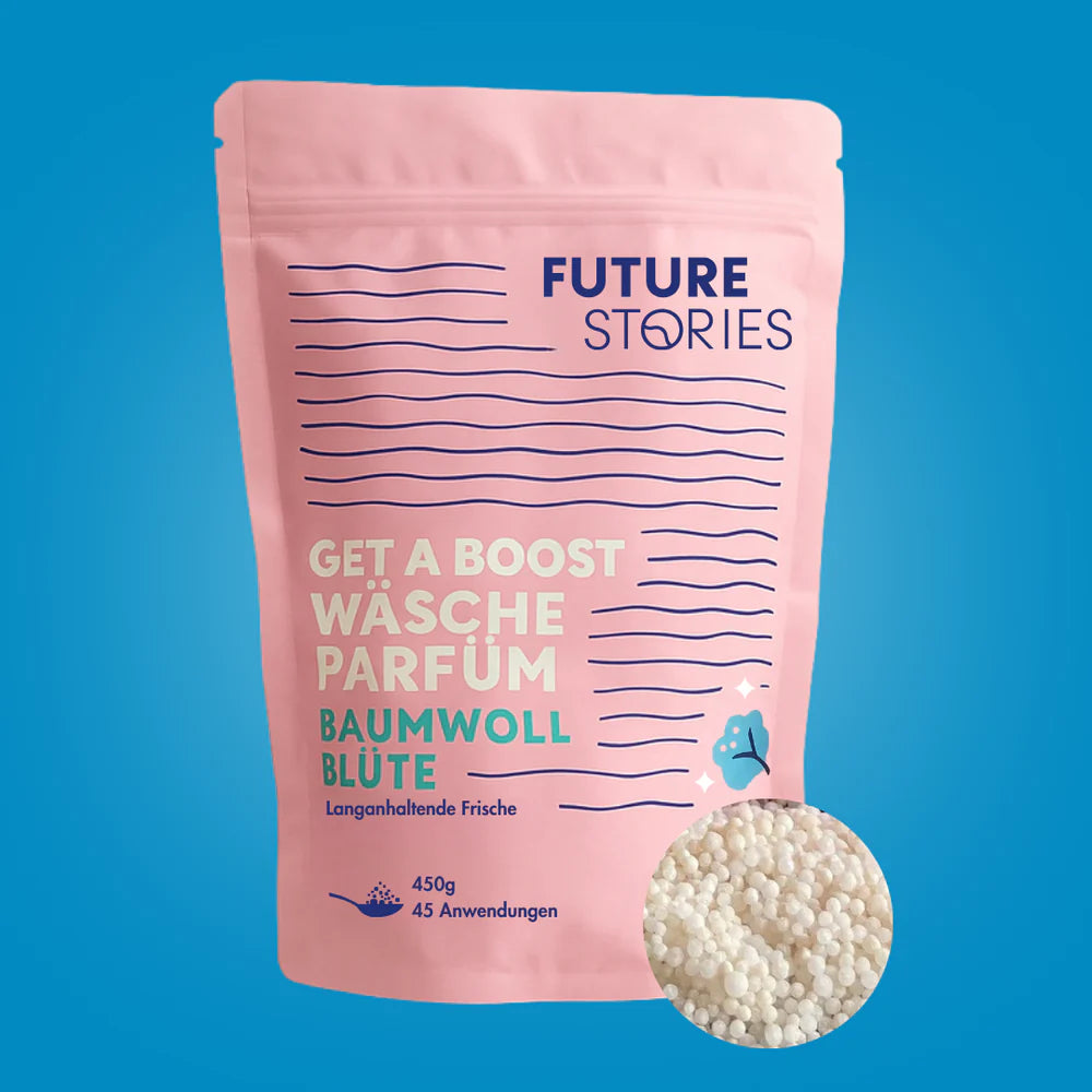 Ein rosafarbener, wiederverschließbarer Beutel mit der Aufschrift Future Stories enthält Wäscheparfümperlen namens Baumwoll Blüte. In der unteren rechten Ecke ist ein kleiner Stapel weißer Perlen auf blauem Hintergrund zu sehen.
