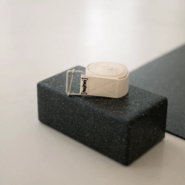 Ein zusammengerollter Yoga-Gurt liegt auf einem schwarzen Yoga-Block neben einer Yoga-Matte.