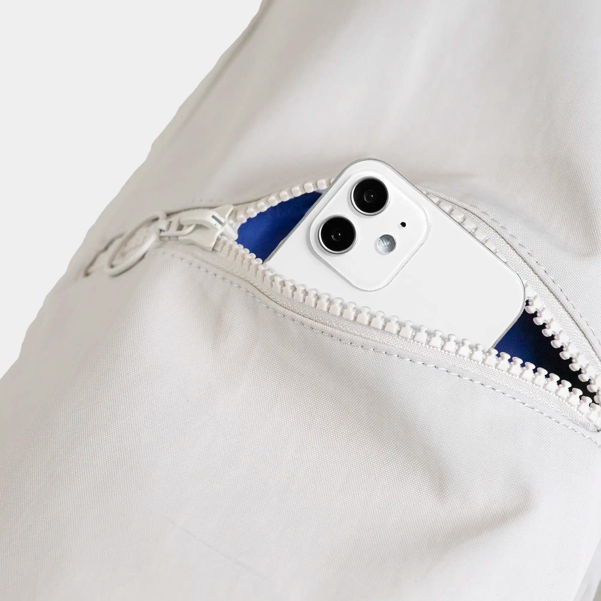Ein weißes Smartphone ragt aus der geöffneten Tasche eines weißen Rucksacks heraus.