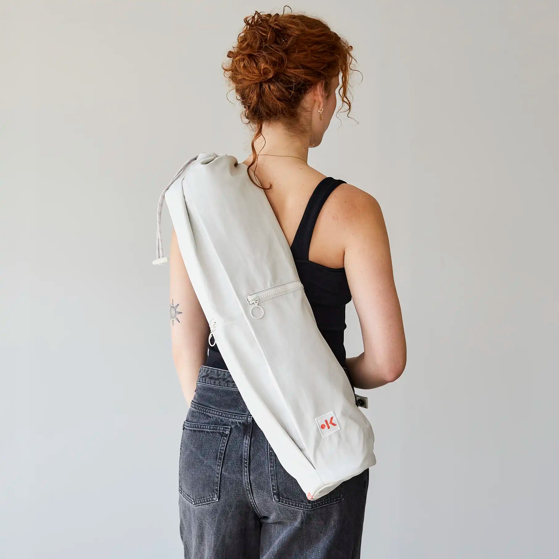 Person mit schwarzen Top und grauer Tasche über der Schulter, steht seitlich mit Blick nach links.