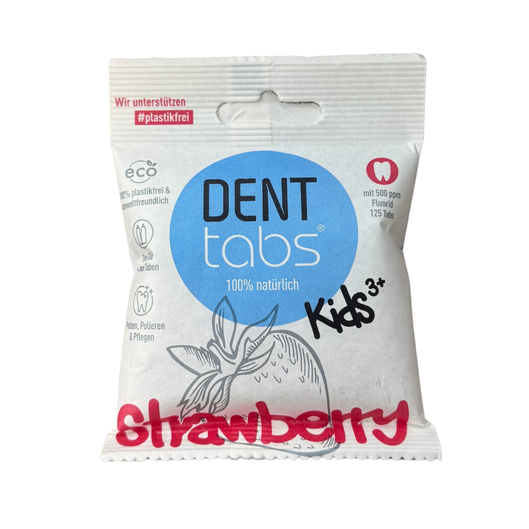 Eine weiße Packung DENT tabs Kids Zahnpastatabletten mit einem blauen Kreislogo, einer Erdbeerillustration und einem roten Erdbeertext. Die Verpackung weist auf 100% natürlich hin und ist für Kinder ab 3 Jahren geeignet.
