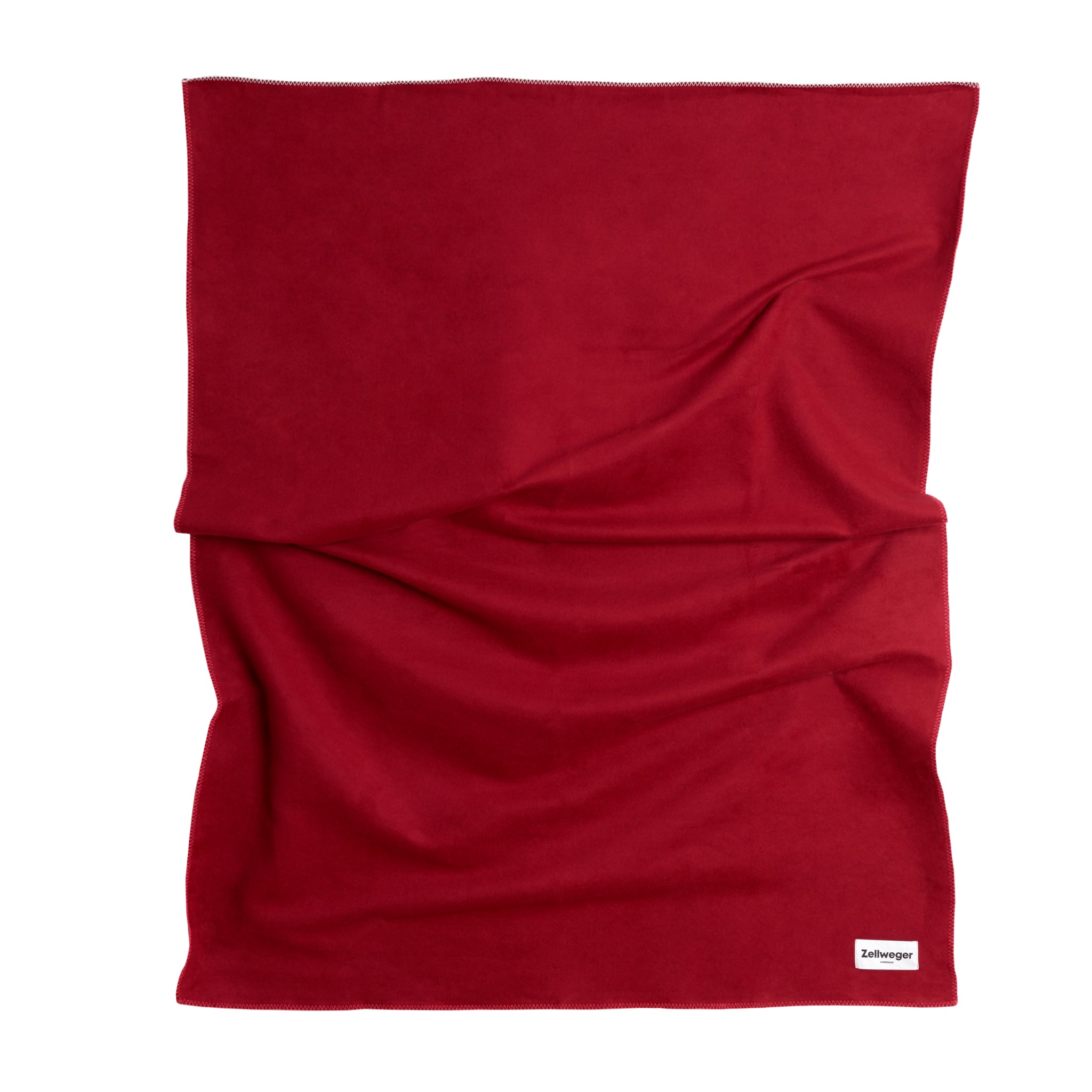 Rote Decke mit leicht gefalteter Struktur, unten rechts ein kleines weißes Etikett mit schwarzer Schrift.