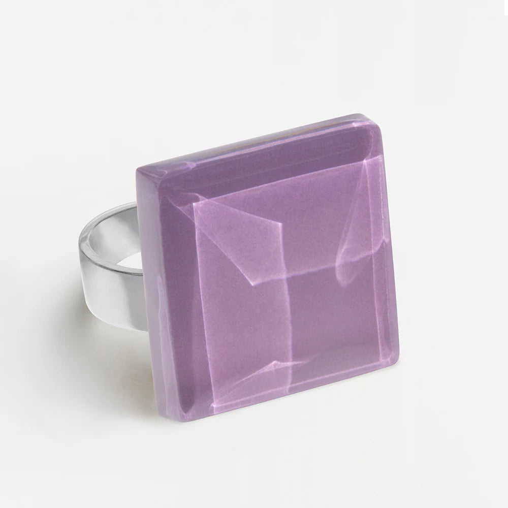 Ein Silberring mit einem großen, quadratischen, facettierten lavendelfarbenen Edelstein mit glänzender Oberfläche auf weißem Hintergrund.
