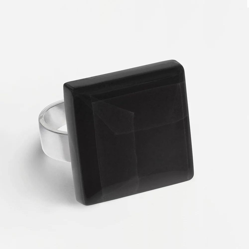 Ein Silberring mit einem großen schwarzen Edelstein im Quadratschliff auf der Oberseite, fotografiert vor einem schlichten weißen Hintergrund.