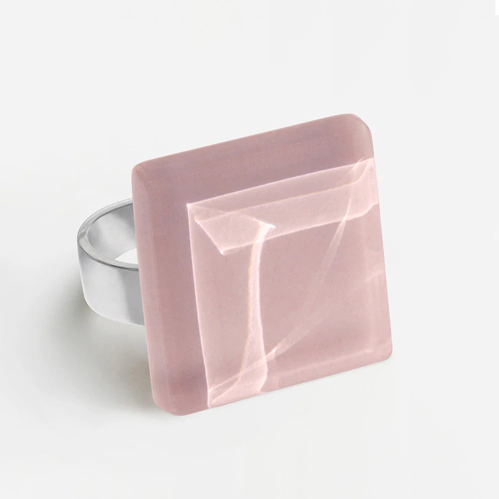 Ein Silberring mit einem großen, quadratischen, pastellrosa Edelstein mit geometrischem, abgeschrägtem Muster auf weißem Hintergrund.