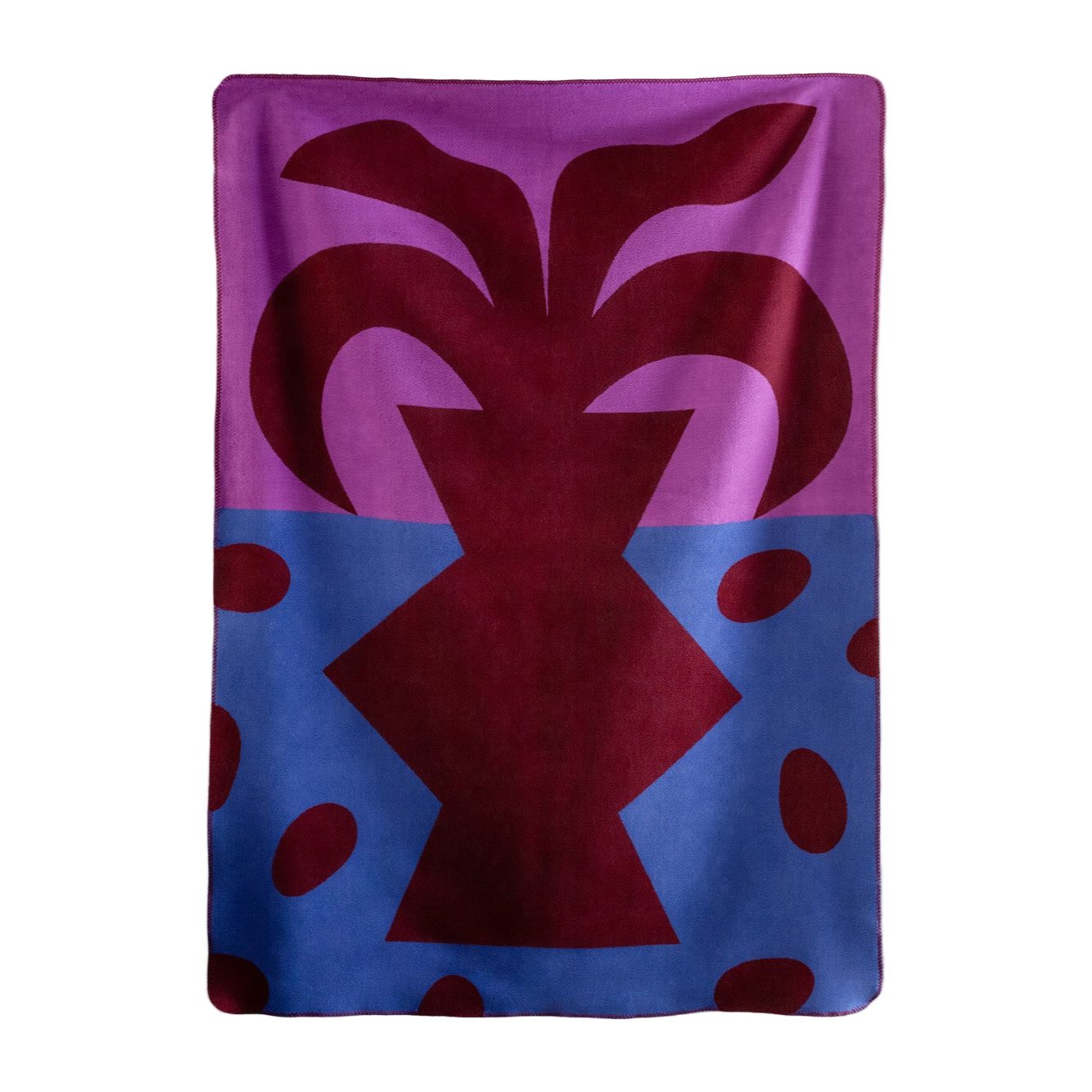 Eine Decke mit dem abstrakten Muster einer dunkelroten Vase mit stilisierten Blättern auf violettem und blauem Hintergrund, akzentuiert durch verstreute rote ovale Formen.