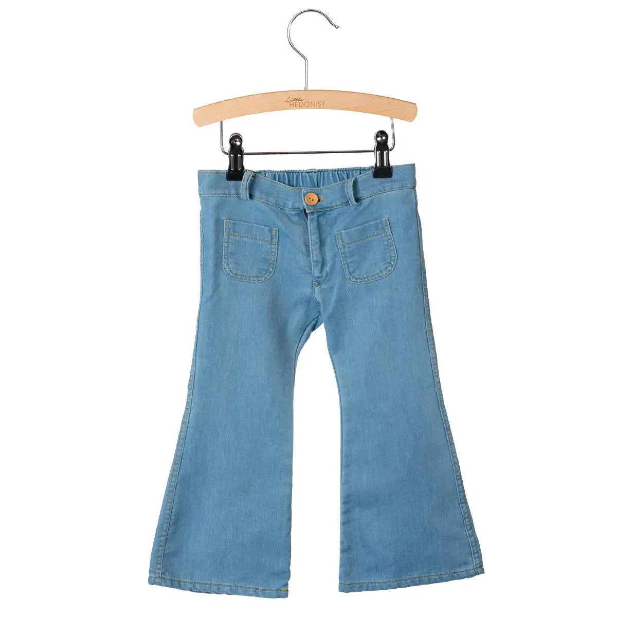 Ein Paar hellblaue Jeans mit Schlag für Kinder, die an einem Holzbügel mit Metallhaken und schwarzen Clips hängen. Die Jeans haben Vordertaschen und einen hellbraunen Knopf am Bund.