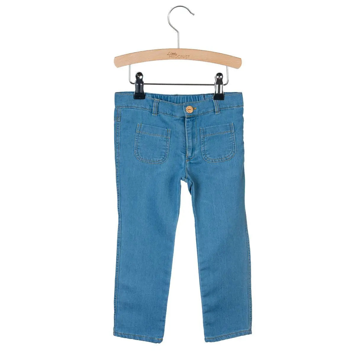 Hellblaue Kinderjeans mit Vordertaschen, ausgestellt auf einem Holzbügel vor weißem Hintergrund.