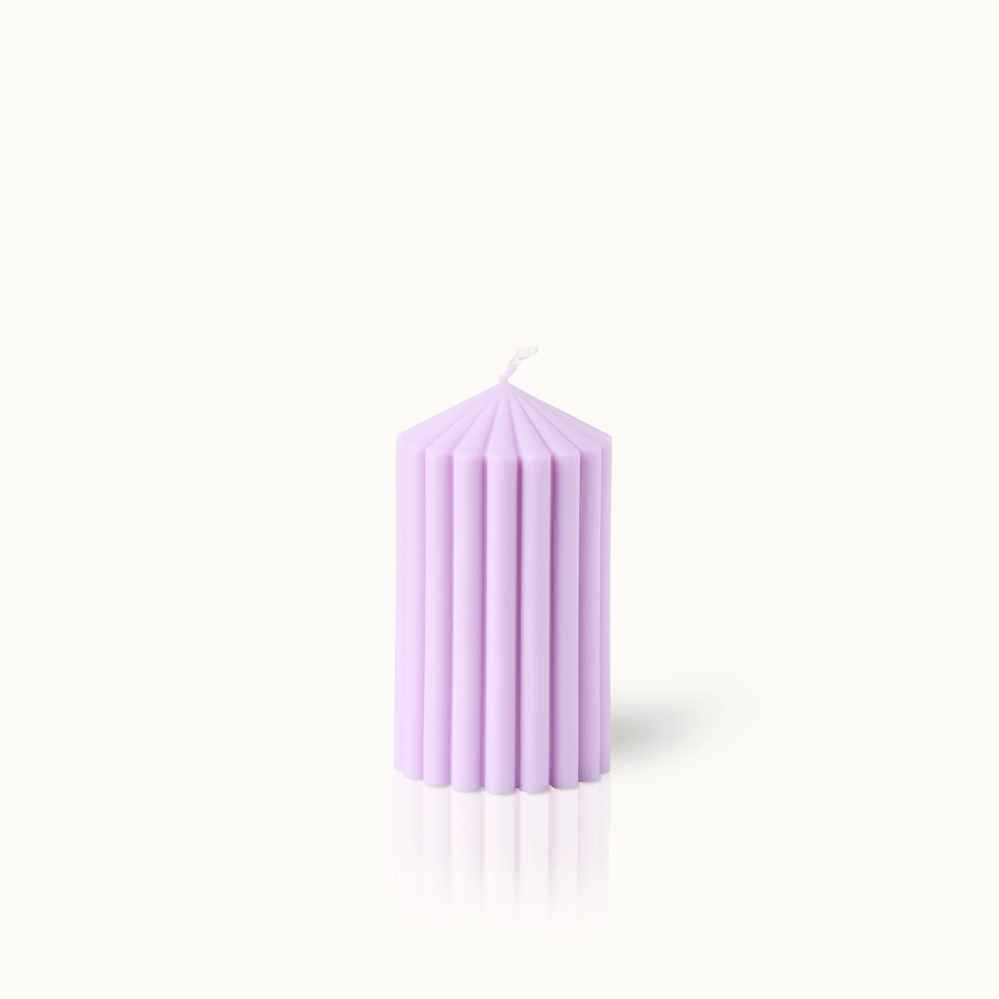 Lila Kerze mit geripptem Design steht auf weißem Hintergrund.