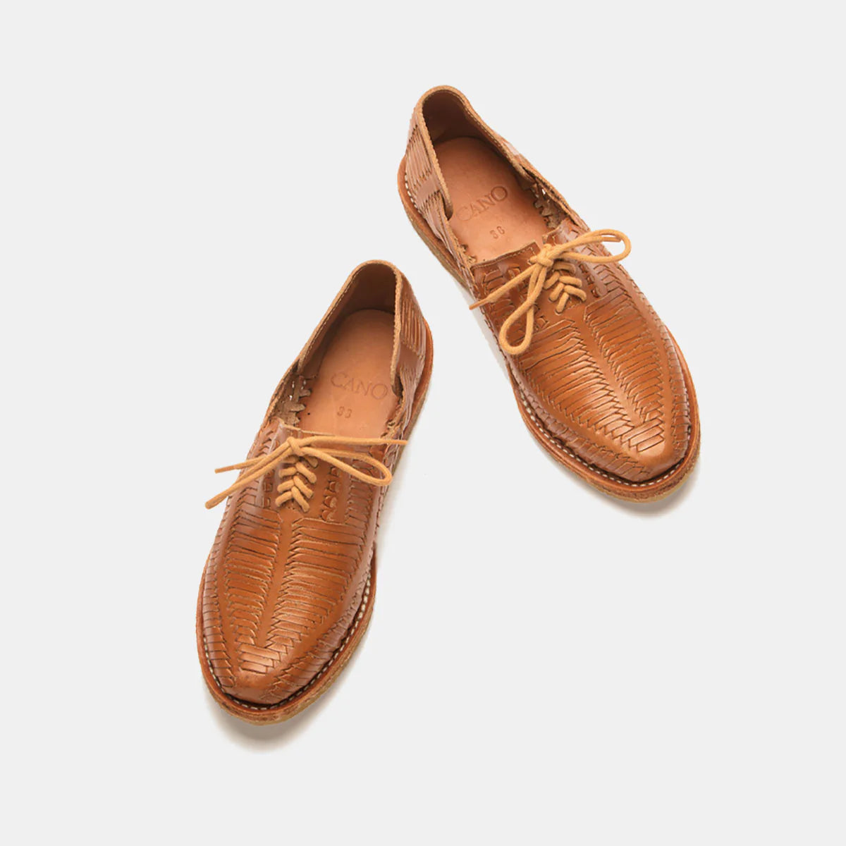 Ein Paar hellbraune, gewebte Lederschuhe mit Schnürsenkeln auf weißem Hintergrund. Die Schuhe haben ein handgefertigtes, strukturiertes Design und eine abgerundete Schuhspitze.