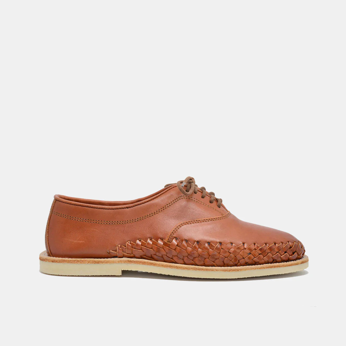 Ein brauner Lederschnürschuh mit einem gewebten Muster an den unteren Seiten, einem glatten Obermaterial und einer beigen flachen Sohle, dargestellt auf einem einfarbig weißen Hintergrund.