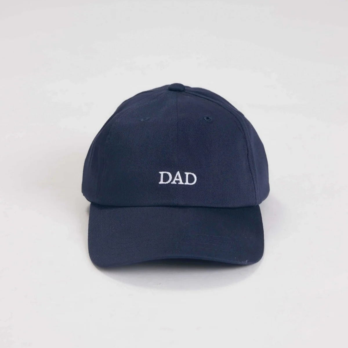 Eine marineblaue Baseballmütze mit dem in weißen Großbuchstaben auf der Vorderseite gestickten Wort DAD, das auf einem weißen Hintergrund steht.