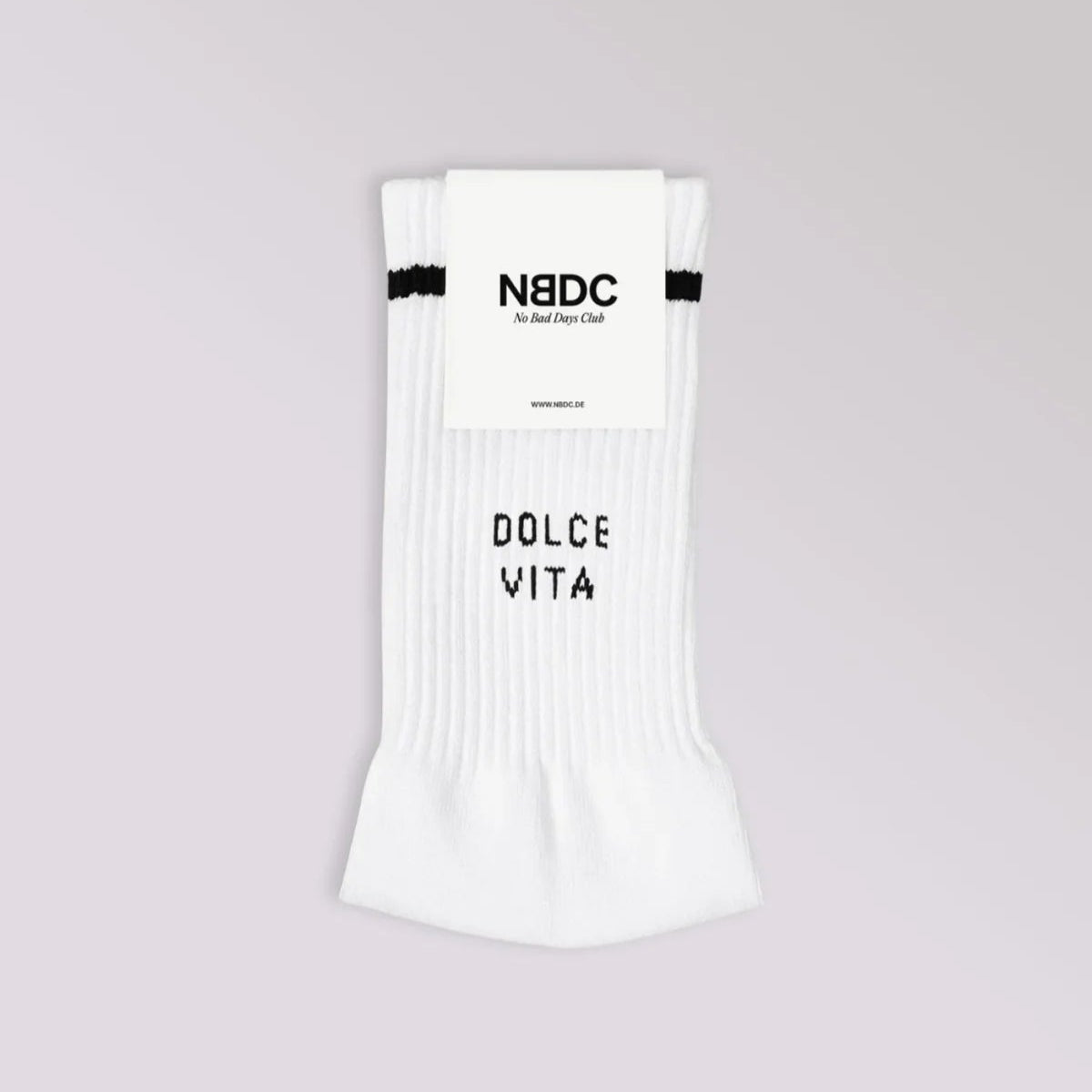 Ein Paar gefaltete weiße Socken mit einem schwarzen Streifen am oberen Ende und dem Aufdruck DOLCE VITA in Schwarz auf der Vorderseite, verpackt mit einem Etikett mit der Aufschrift NBDC. Der Hintergrund ist ein heller Farbverlauf.