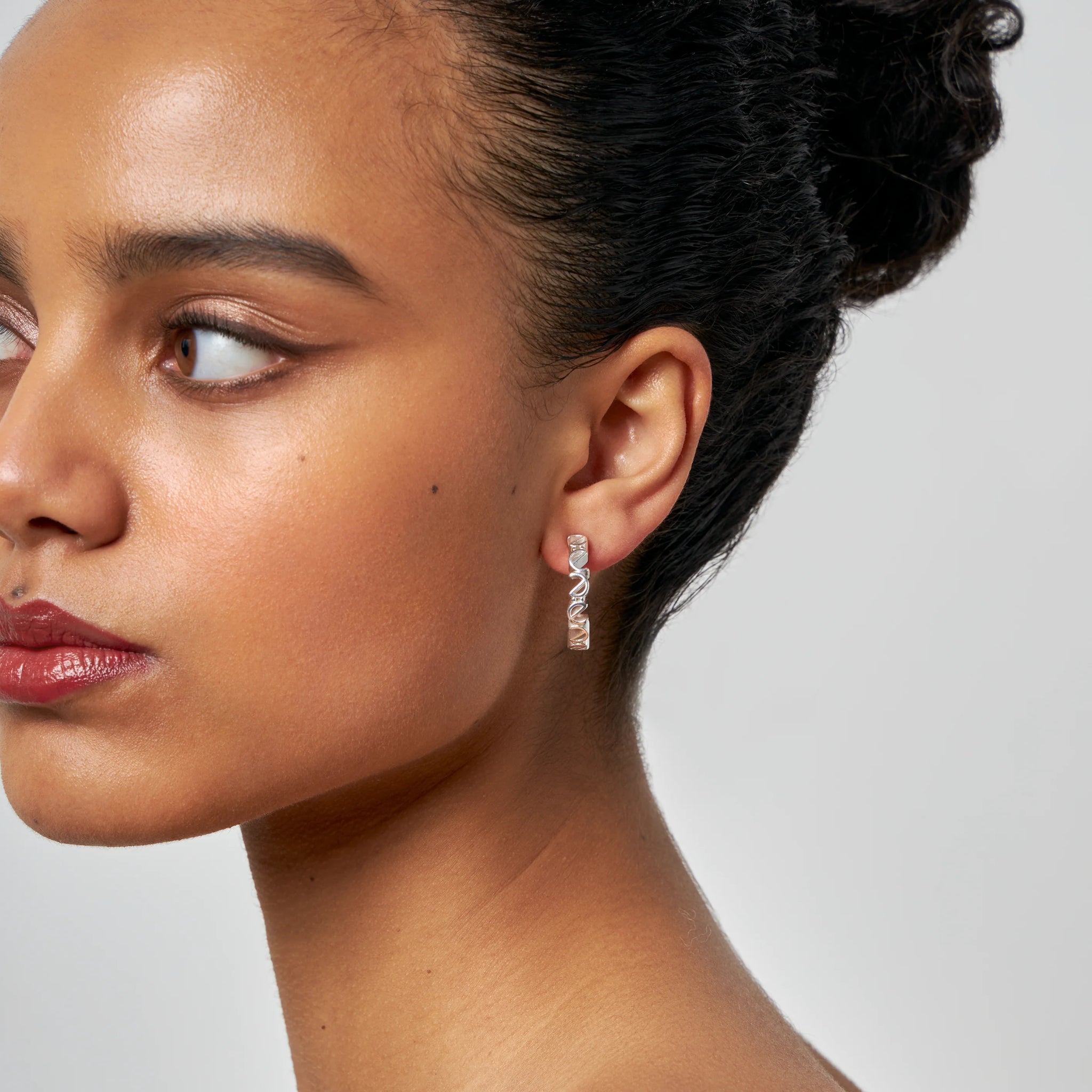 Frau in Nahaufnahme mit attraktivem Ohrring, schaut zur Seite, vor einem neutralen Hintergrund.