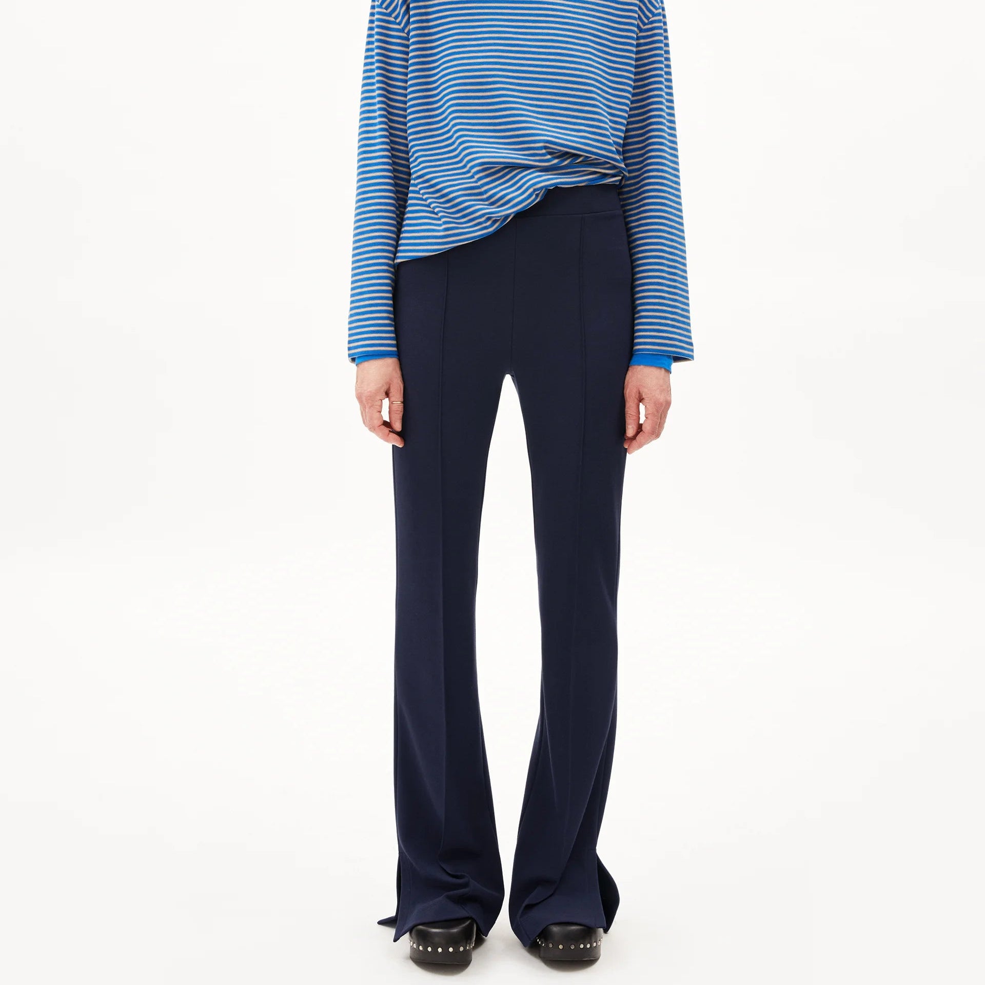 Eine Person, die ein blau gestreiftes langärmeliges Hemd, eine dunkelblaue Schlaghose, schwarze Schuhe, einen blauen Rollkragenpullover und eine blaue Baseballmütze trägt, steht vor einem schlichten weißen Hintergrund.