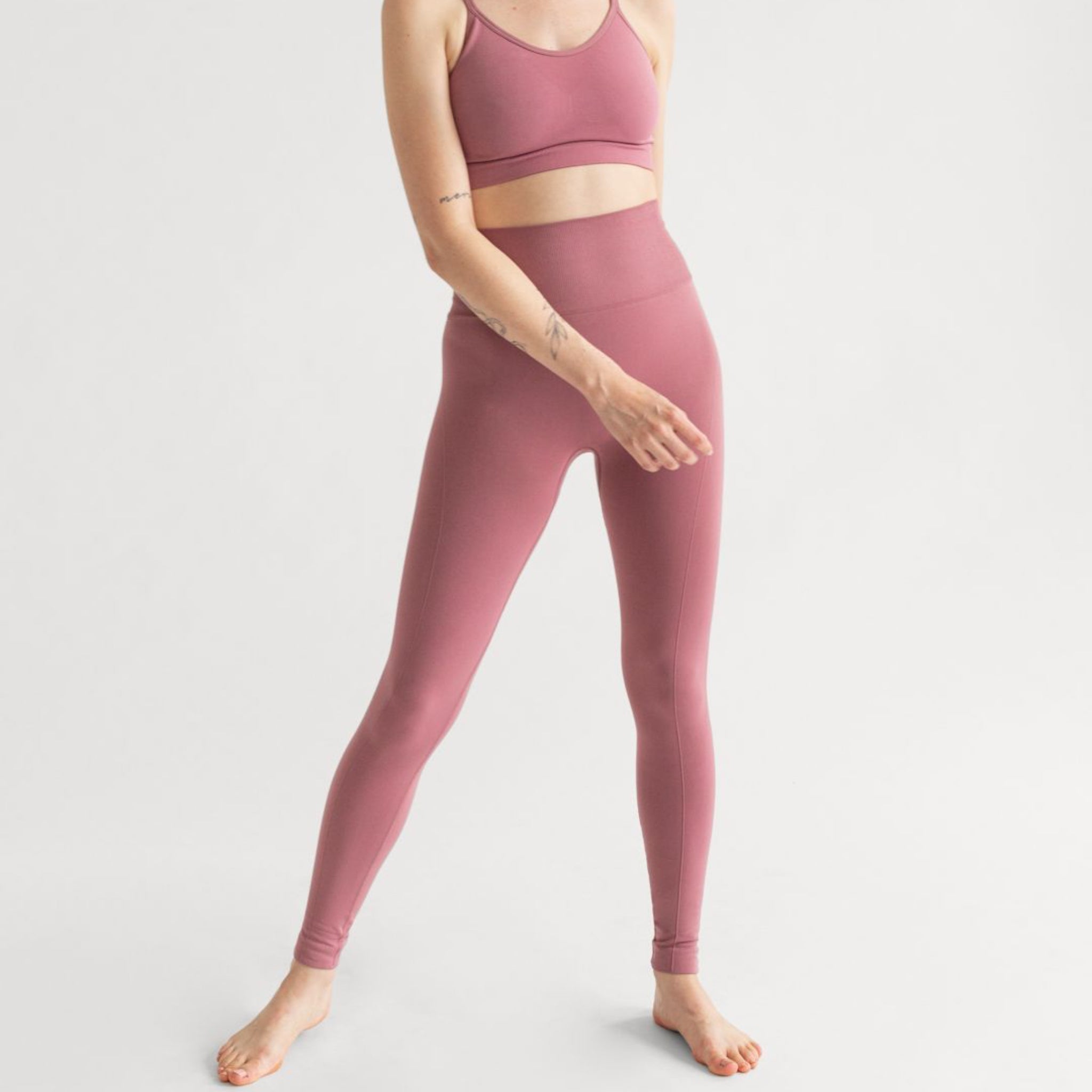 Person in pink workout leggings and a sports bra standing barefoot against a plain background.