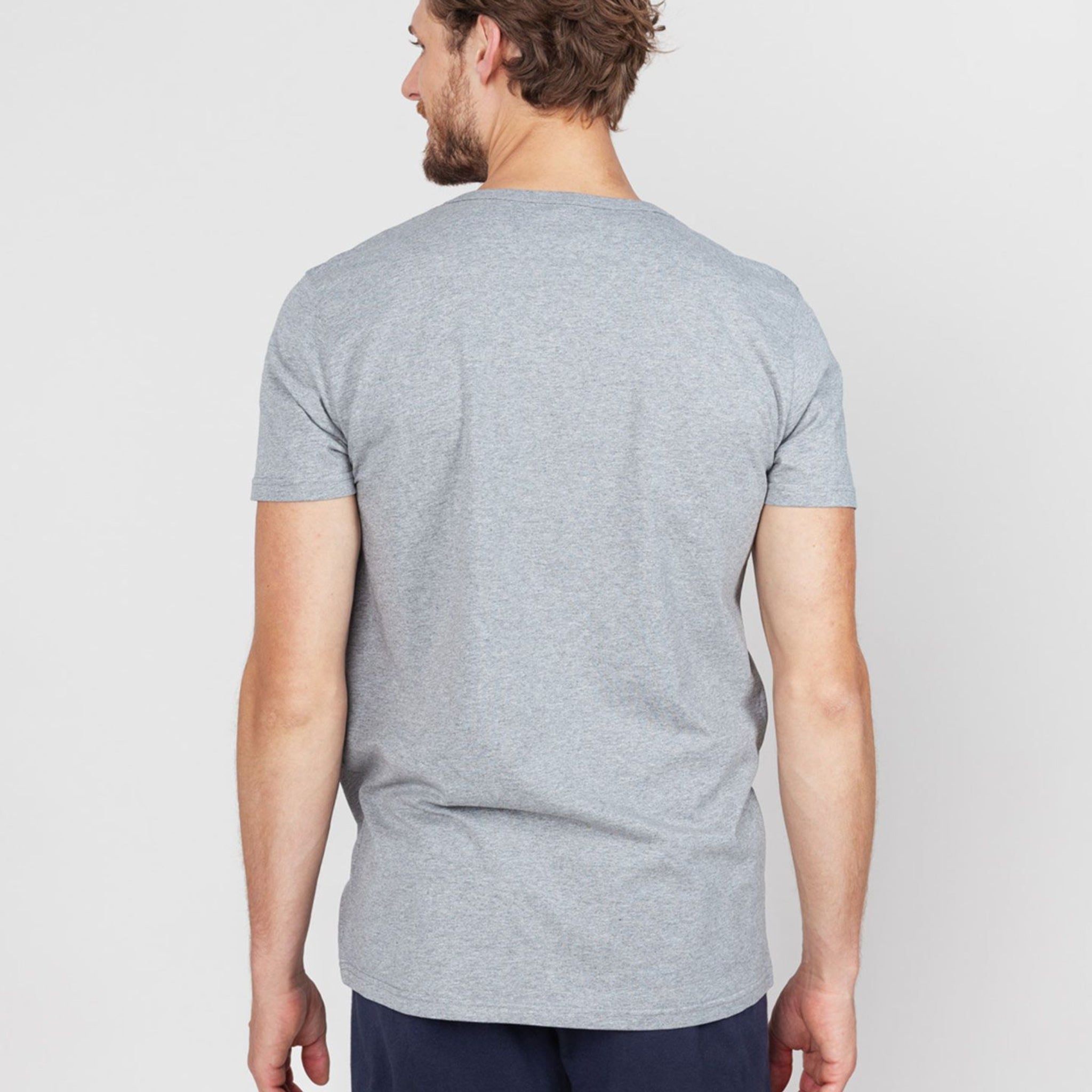 Ein Mann steht mit dem Rücken zur Kamera und trägt ein graues T-Shirt und dunkle Hosen.