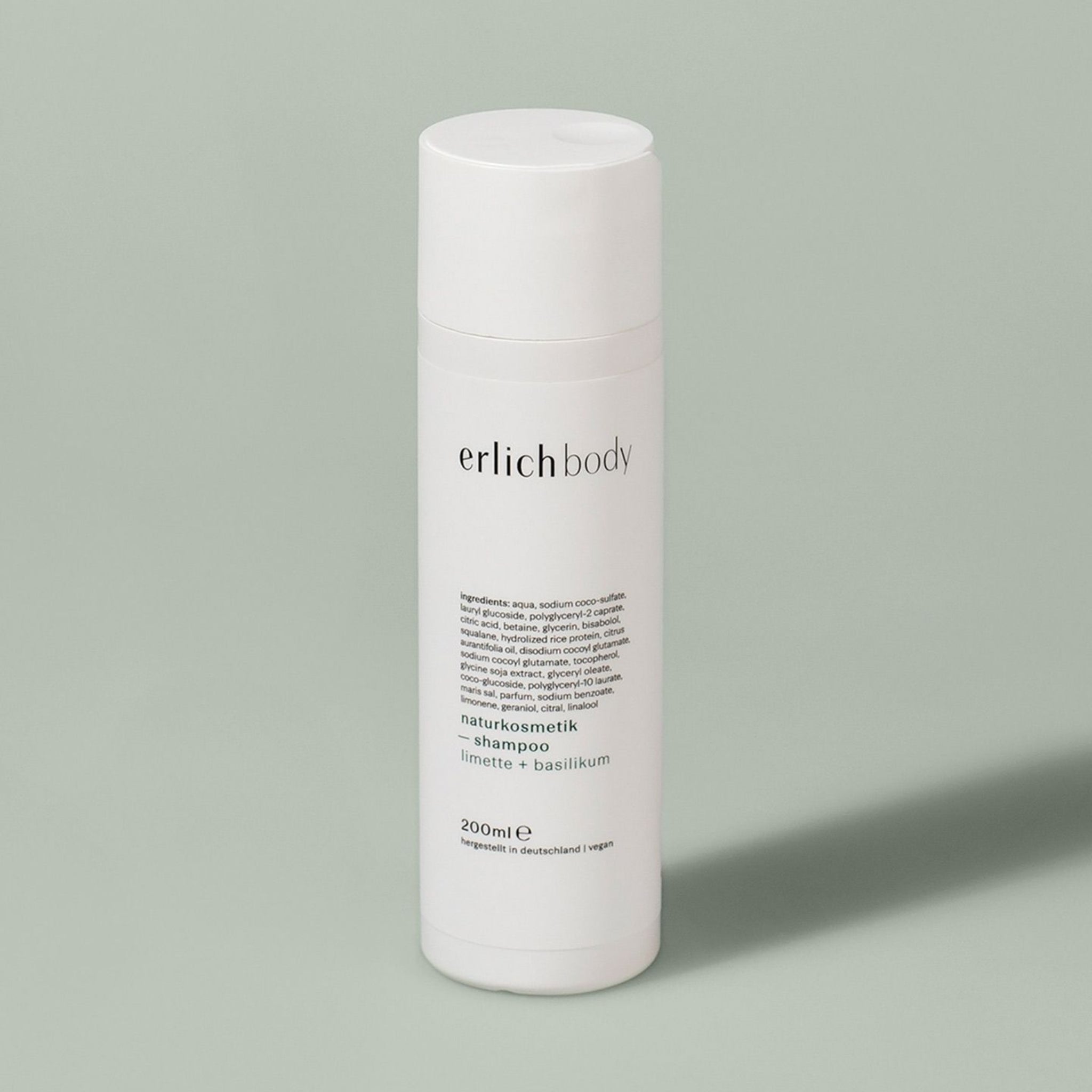 Weiße Shampoo-Flasche von "erlich body" mit Limette- und Basilikumduft auf grauem Hintergrund.