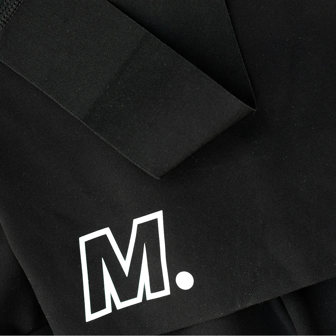 Eine Nahaufnahme von schwarzem Stoff mit großen schwarzen Bändern und einem fetten weißen Buchstaben M, gefolgt von einem Punkt in der unteren Ecke.