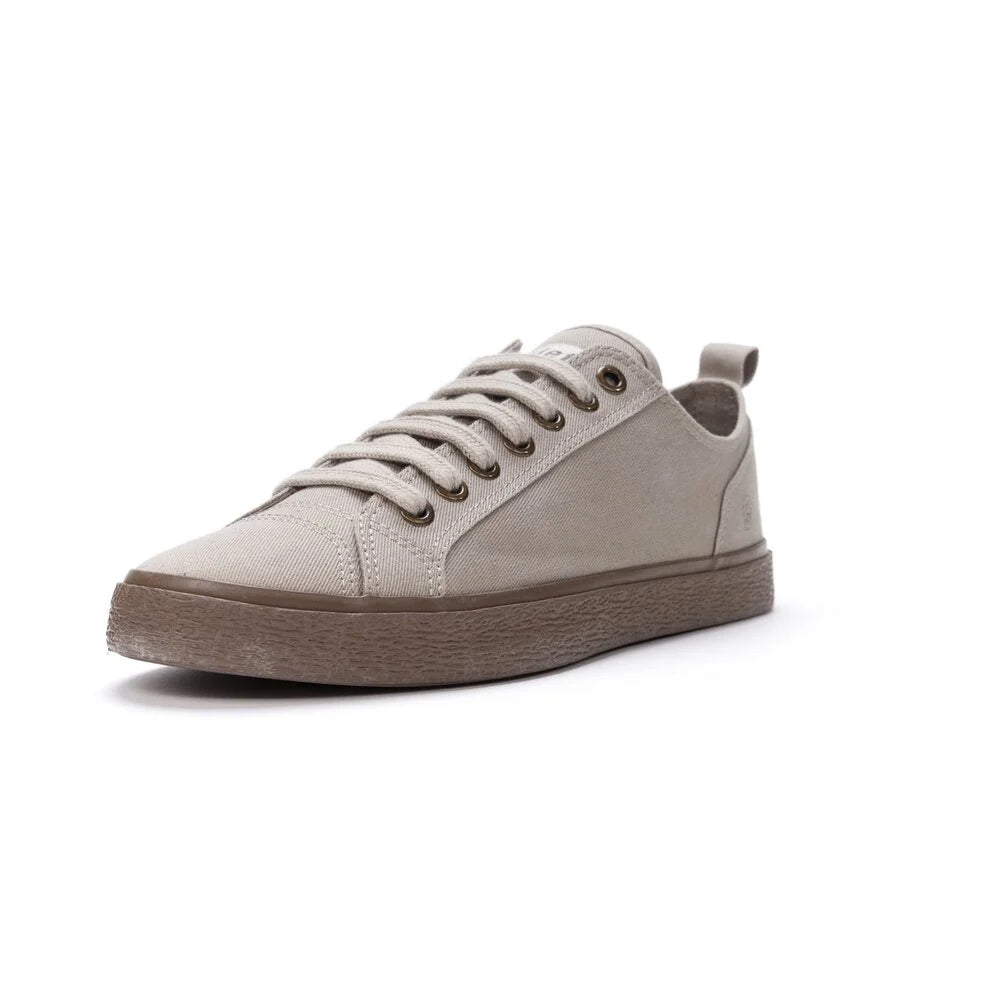 Ein beiger Low-Top-Sneaker mit brauner Gummisohle und beigen Schnürsenkeln, von vorne gesehen auf einem weißen Hintergrund.