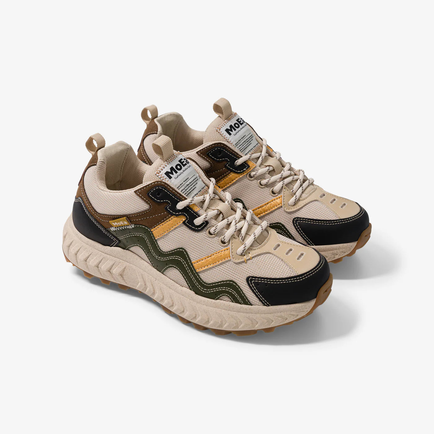 Ein Paar beige, schwarze, olivgrüne und senfgelbe Sneaker mit gewellten Designdetails, dicken strukturierten Sohlen und MoEa-Branding auf der Zunge auf weißem Hintergrund.