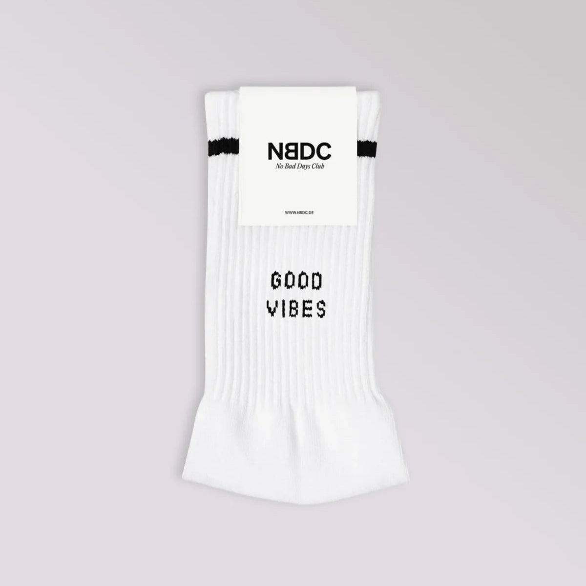Ein Paar weiße Socken mit einem schwarzen Streifen am oberen Ende und der Aufschrift GOOD VIBES in schwarz. Die Socken haben ein Etikett mit der Aufschrift NBDC No Bad Days Club. Der Hintergrund ist hellgrau.