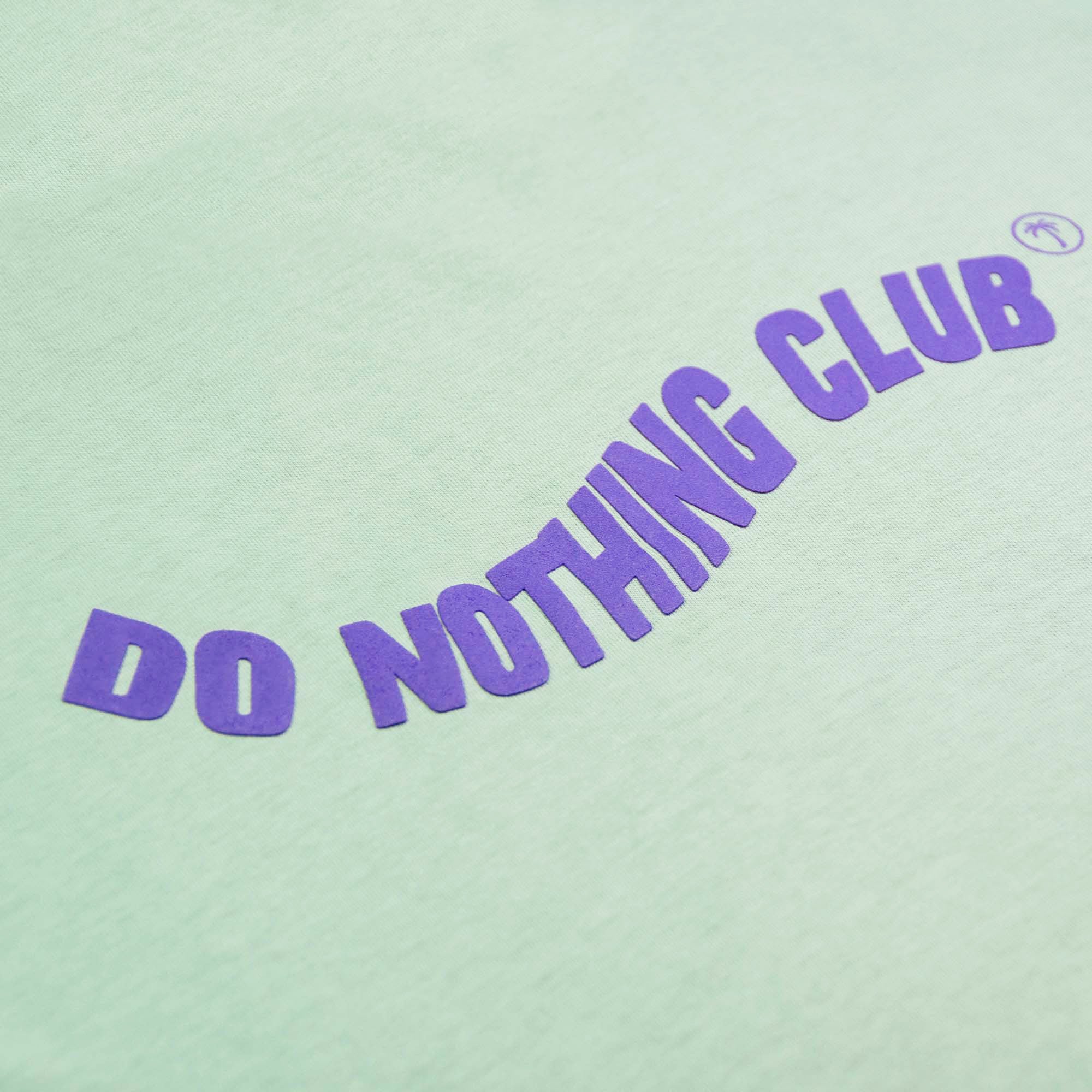 Grünes T-Shirt mit dem lila Schriftzug "DO NOTHING CLUB" und einem kleinen Palmensymbol.