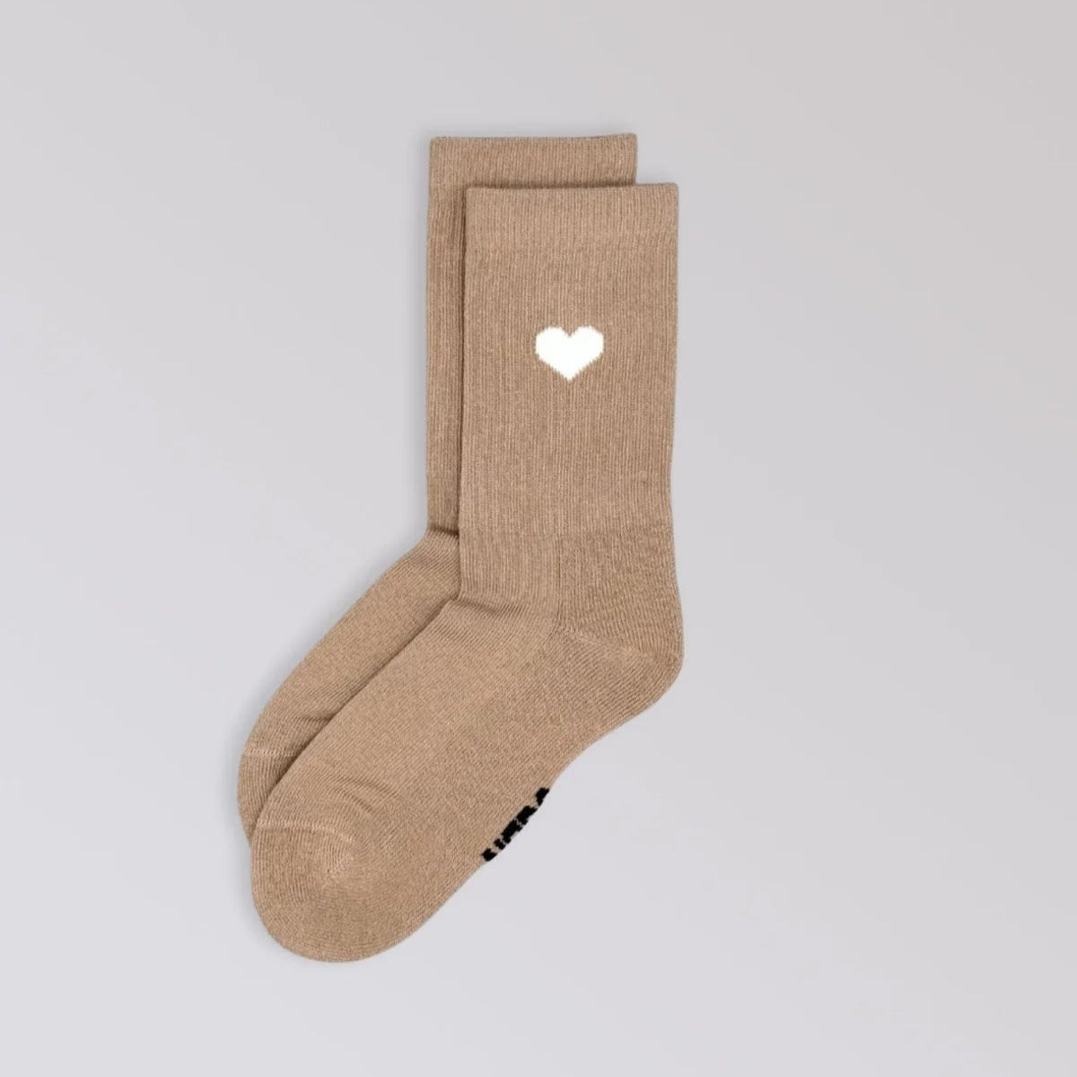 Ein Paar beigefarbene Socken mit einem weißen Herzmotiv am oberen Rand auf einem schlichten hellgrauen Hintergrund.