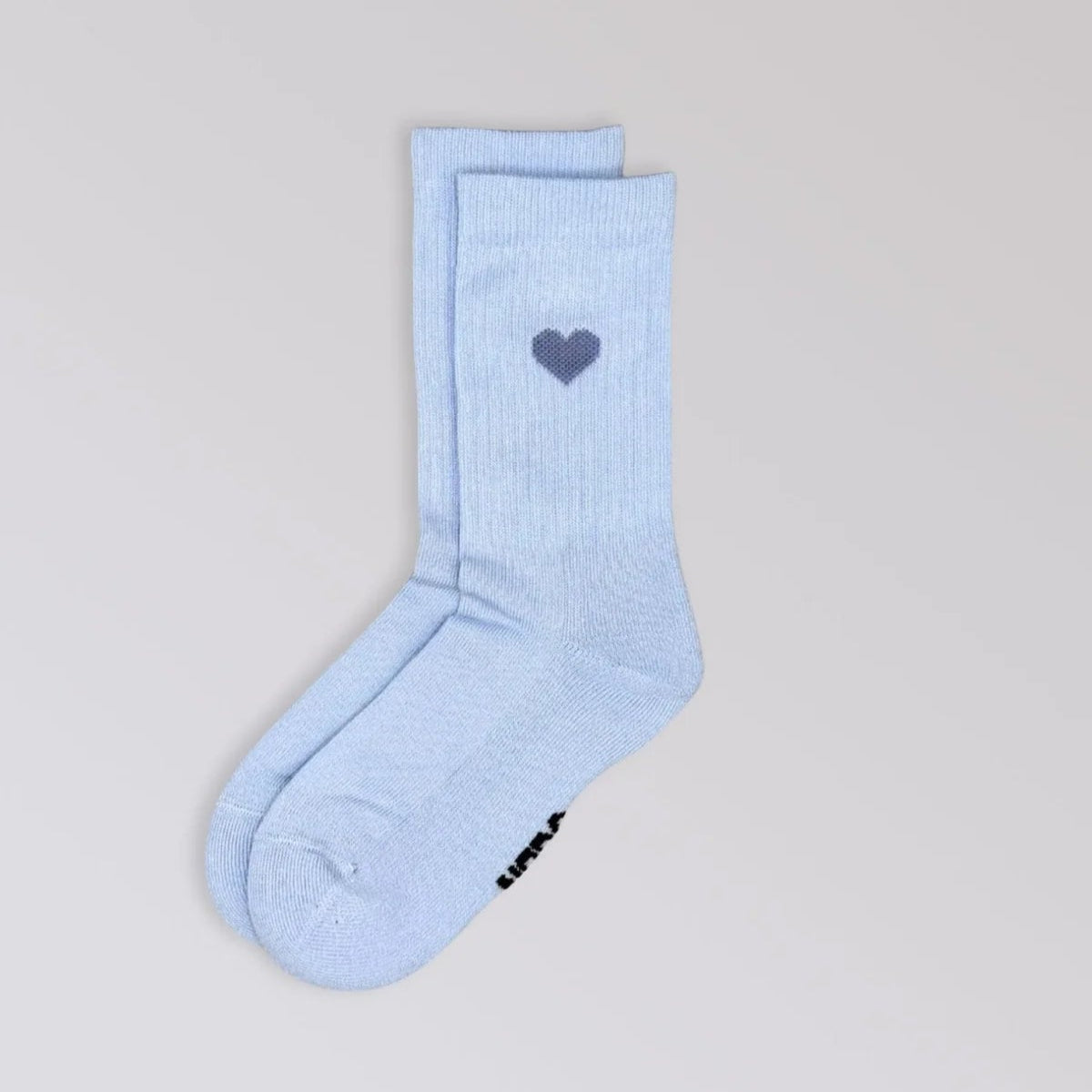 Ein Paar hellblaue Socken mit einem kleinen dunkelblauen Herzmotiv am oberen Rand. Die Socken sind flach auf einen hellgrauen Hintergrund gelegt.
