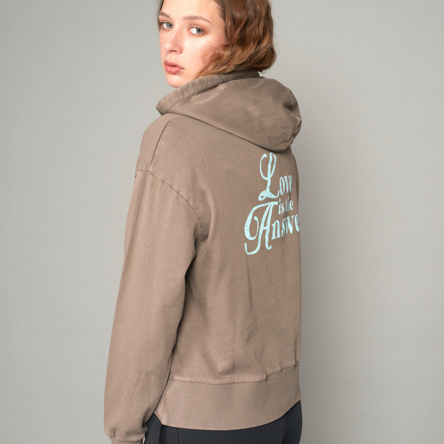 Frau in braunem Hoodie mit dem Rücken zur Kamera, Schriftzug "Love is the Answer" auf dem Rücken.